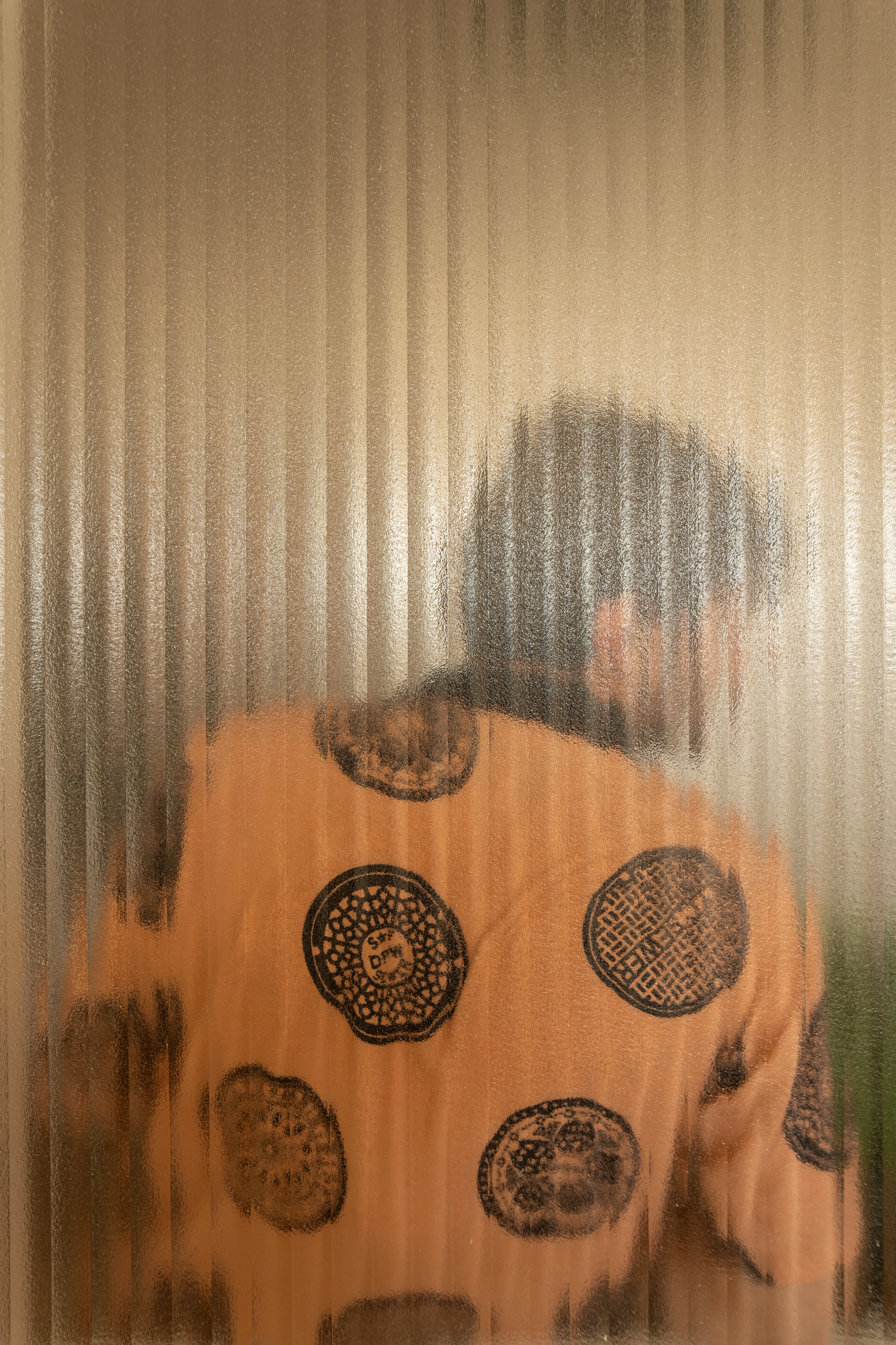 Untitled Office — a figure in a patterned orange shirt seen through ribbed glass