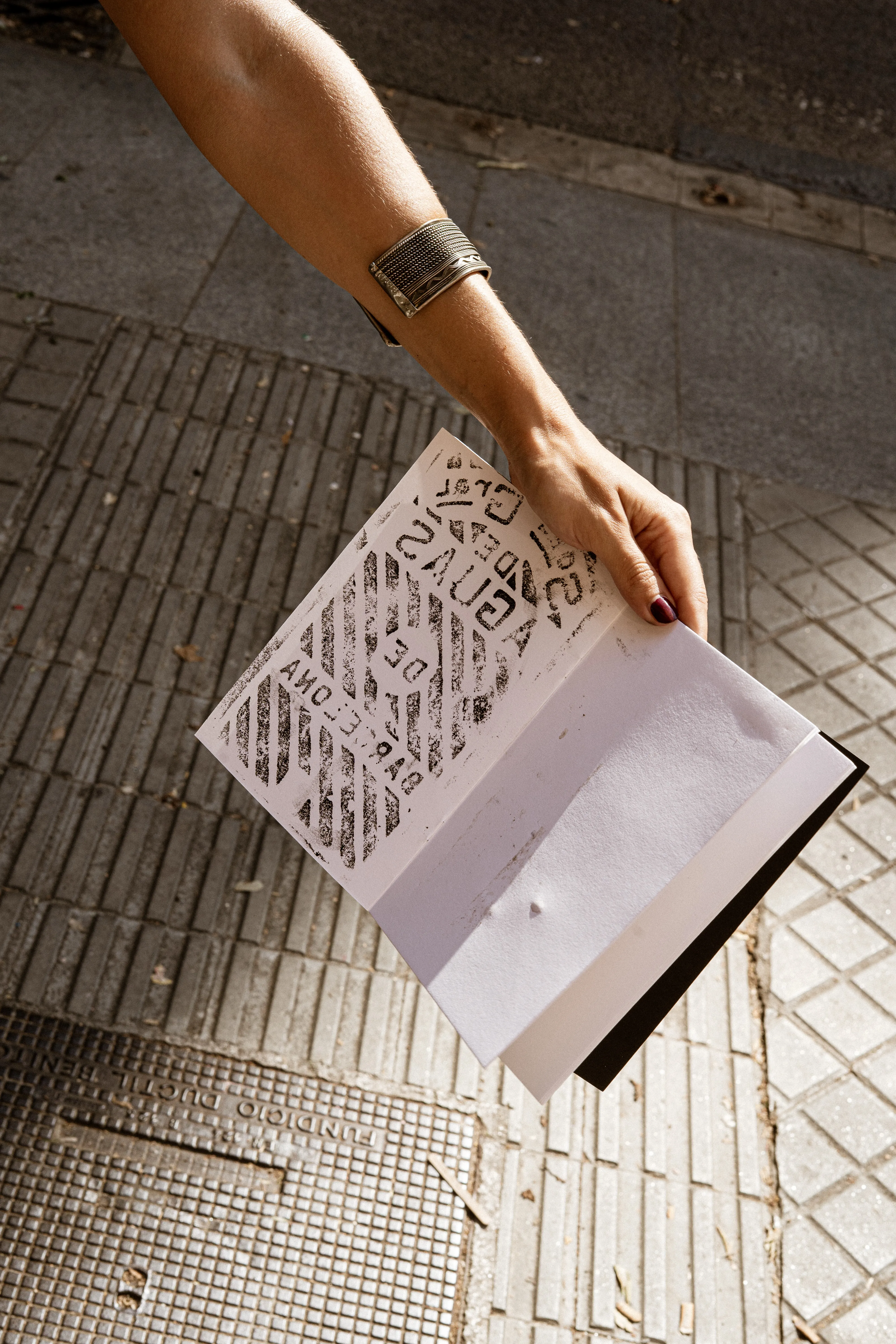 An outstretched arm holding up a paper rubbing of a manhole cover above a tiled pavement