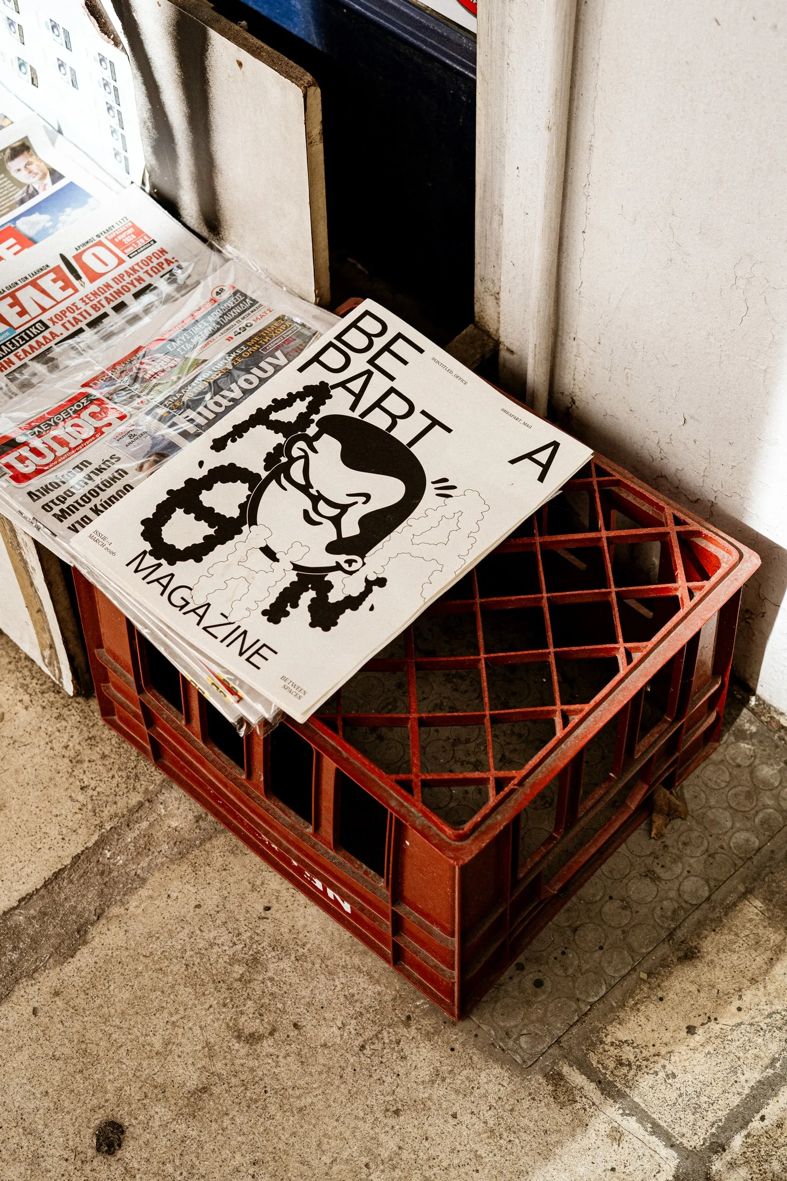The magazine on a red plastic crate beside a newspaper kiosk