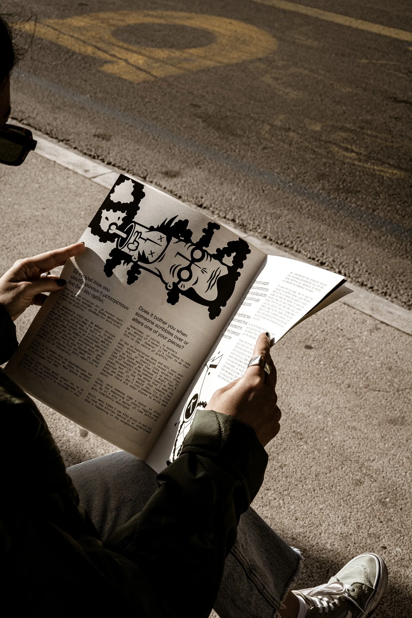 Someone sitting on the kerb reading an illustrated magazine spread