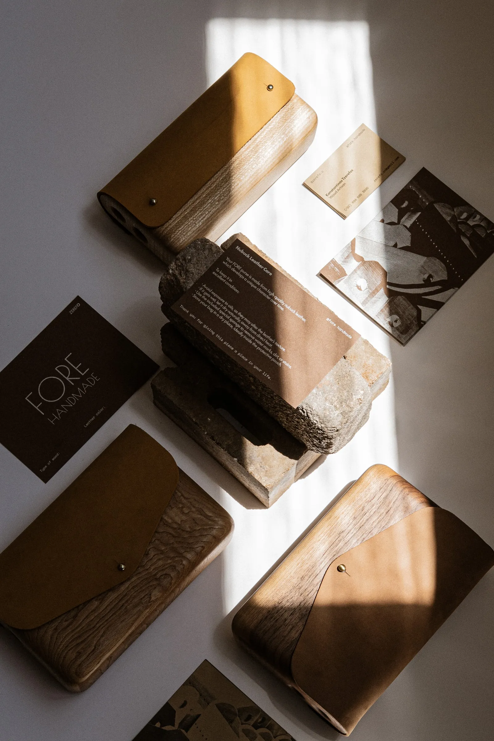 Flat lay of wood-and-leather FORE bags, printed cards and a stone in a band of sunlight