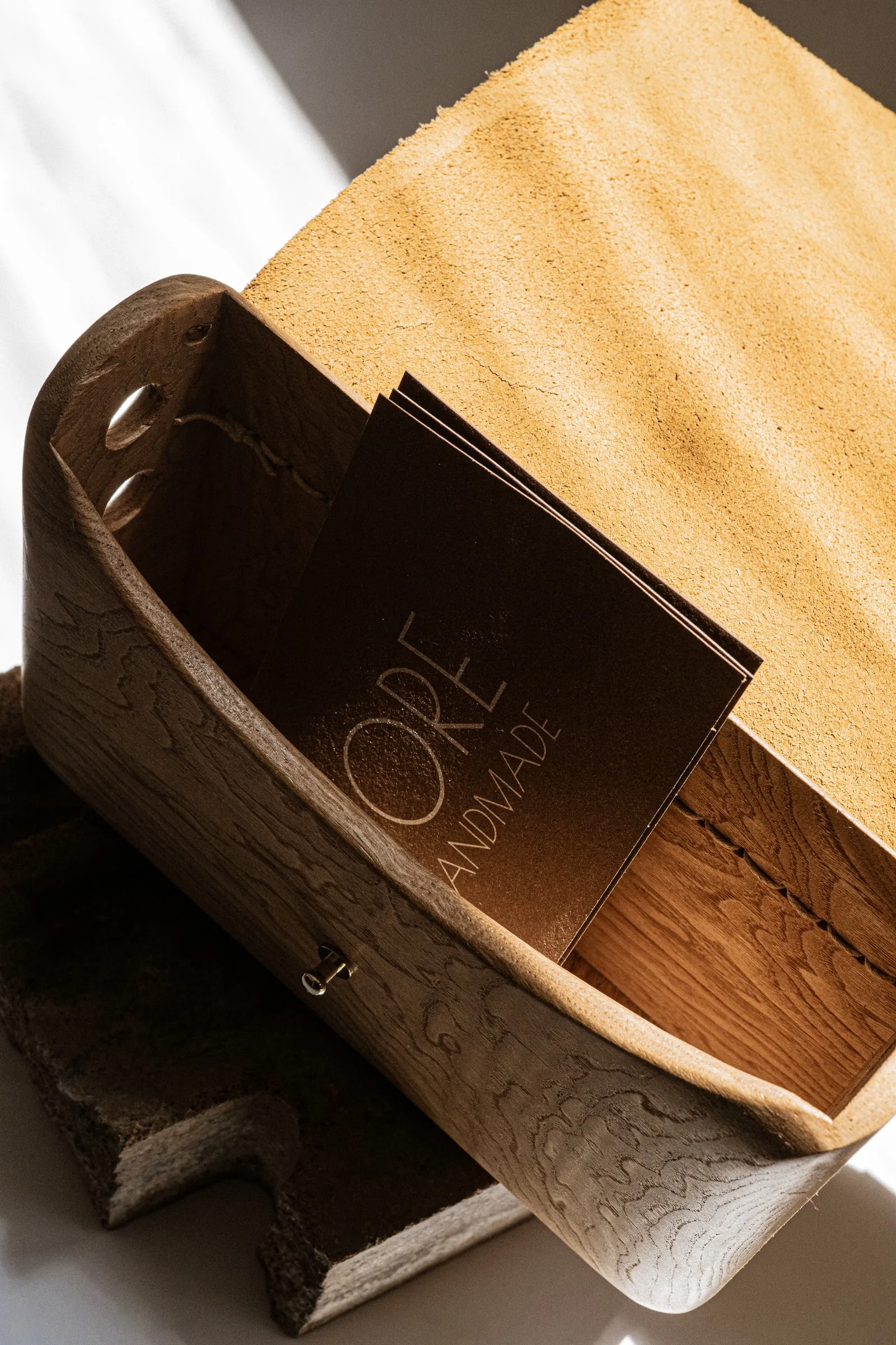 A curved wooden bag with a suede flap holding a dark FORE HANDMADE card