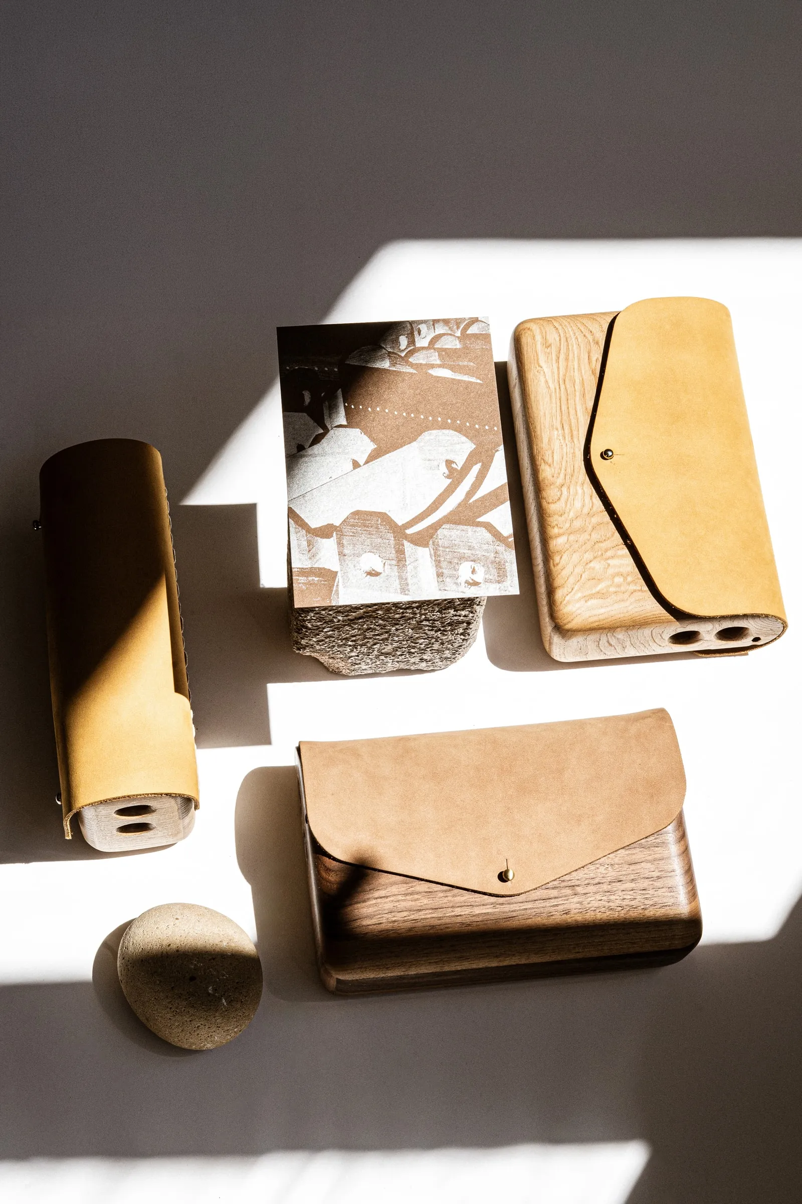 Three wood-and-leather bags arranged with an illustrated card and a round stone