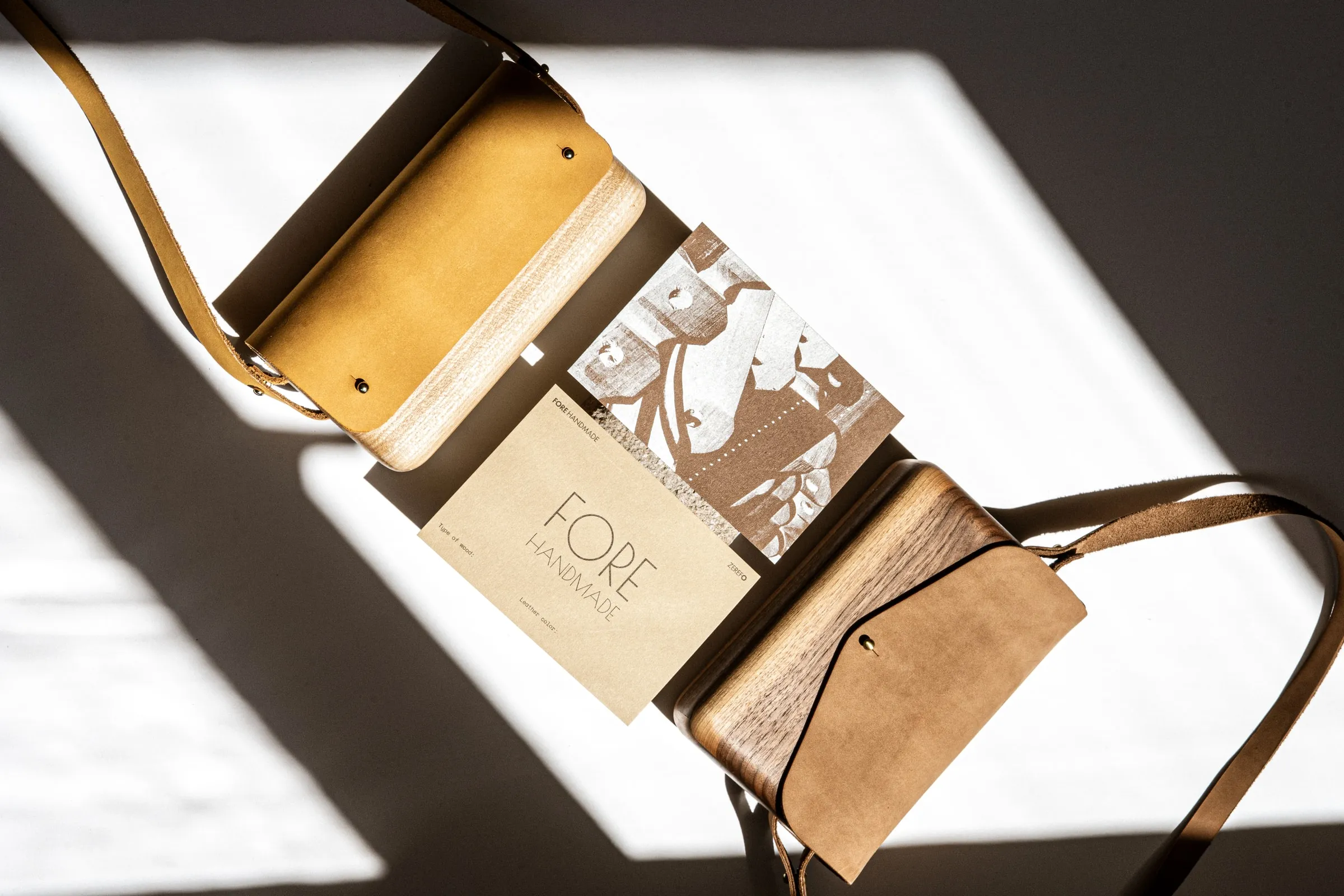 Two wooden bags with leather straps framing a FORE HANDMADE card in sunlight