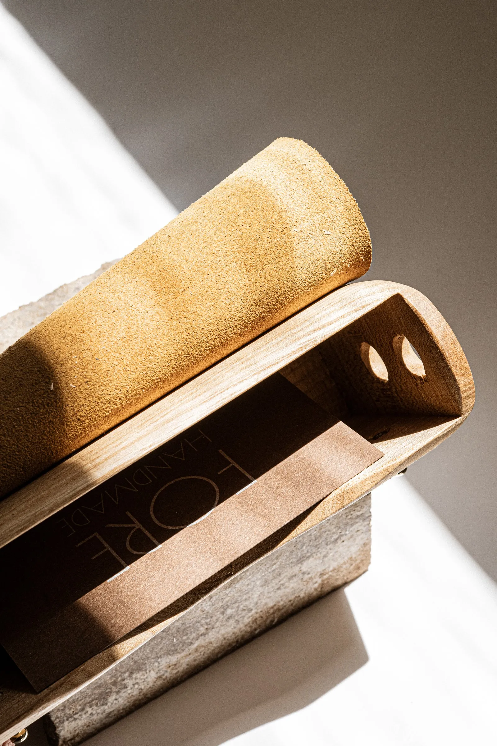 A curved wooden bag with a suede flap, the FORE lettering inside, in a beam of light