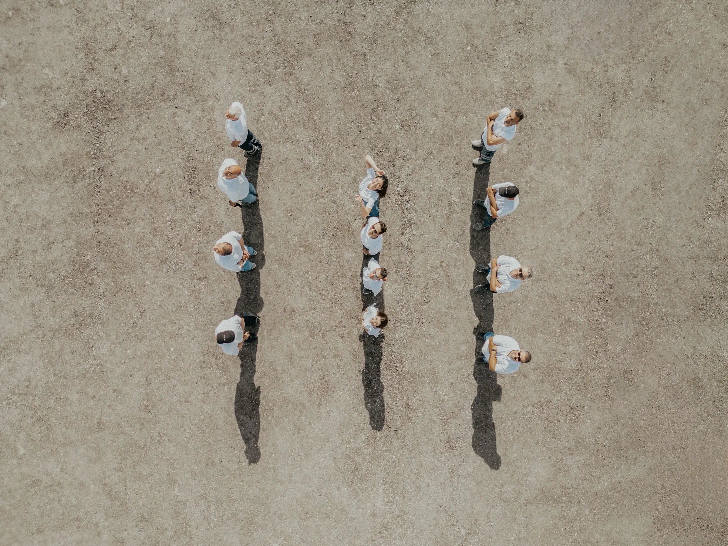 Aerial view of three straight lines of people in white shirts standing on bare concrete