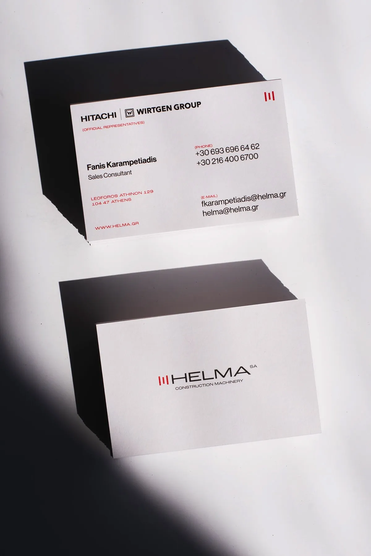 White Helma business cards stacked on black card blocks against a white wall