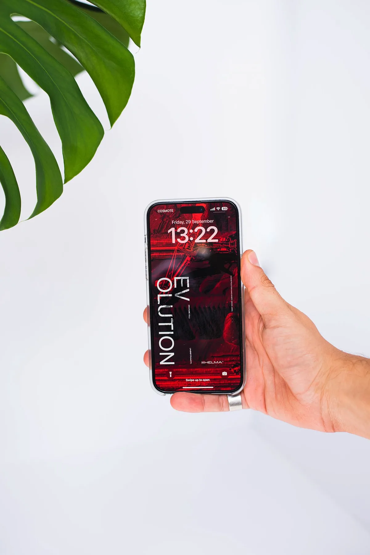 A hand holding a phone showing a red EVOLUTION lock screen, a monstera leaf behind