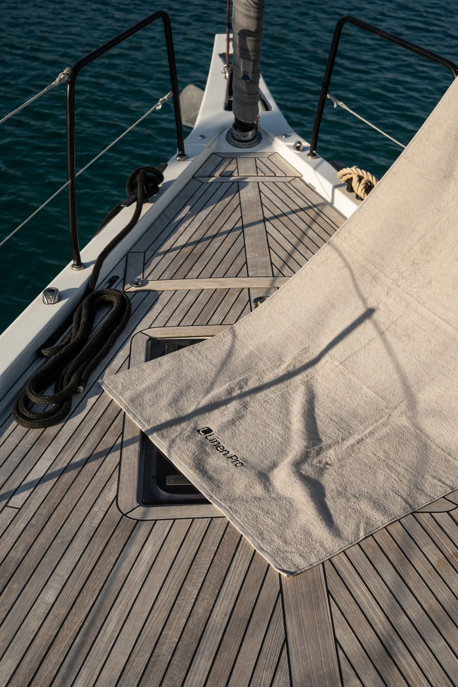 A linen towel with the Linen Pro logo draped across the teak deck of a yacht