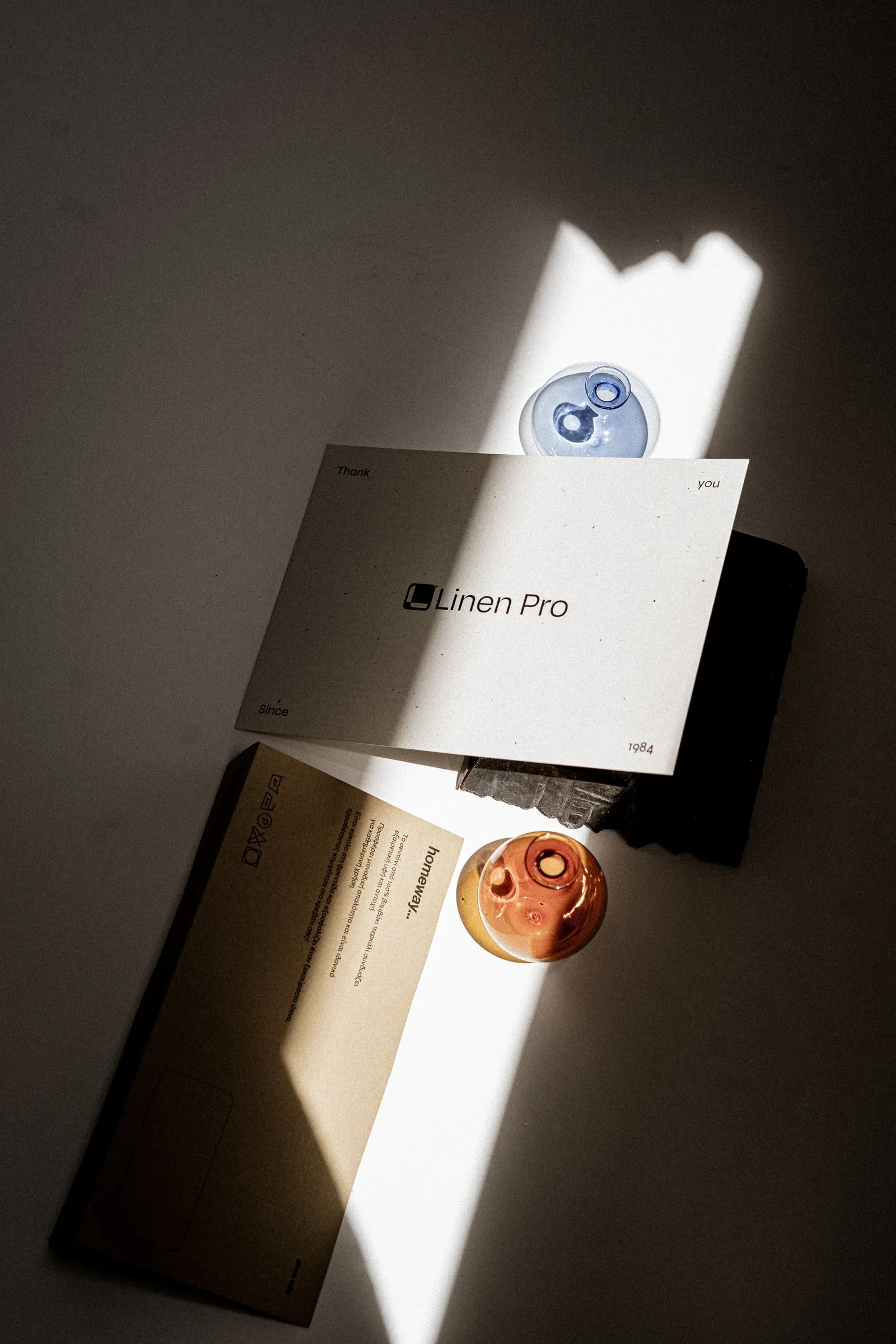 A Linen Pro card and a kraft folder on a dark surface beside glass globes, in raking light