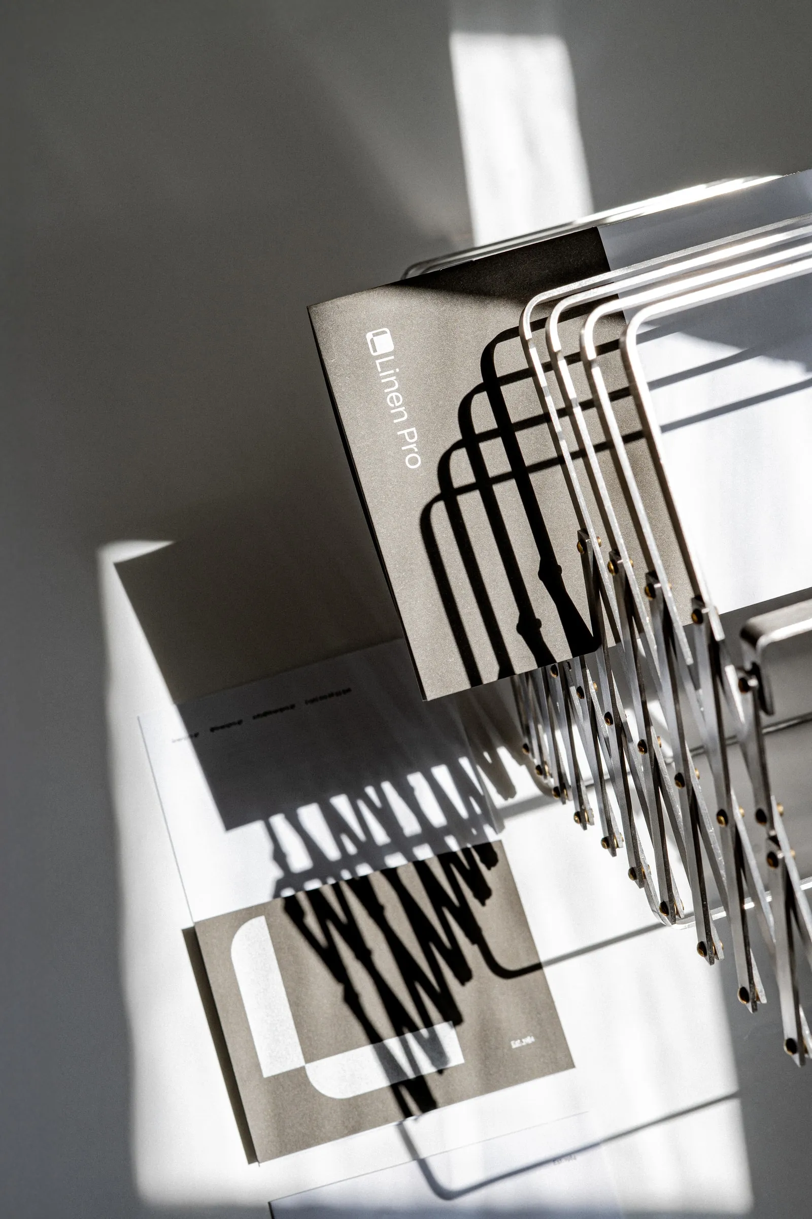A grey Linen Pro folder leaning against a wire rack, its shadow striping the paper