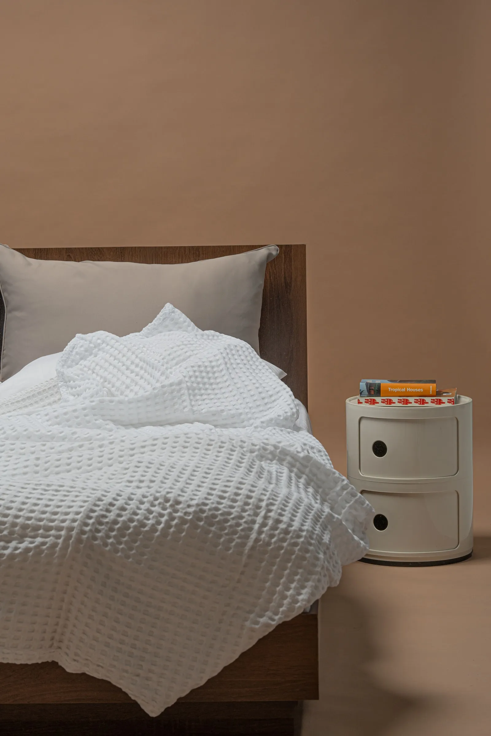 White waffle-weave linen on a bed next to a cream bedside unit, against a warm beige wall