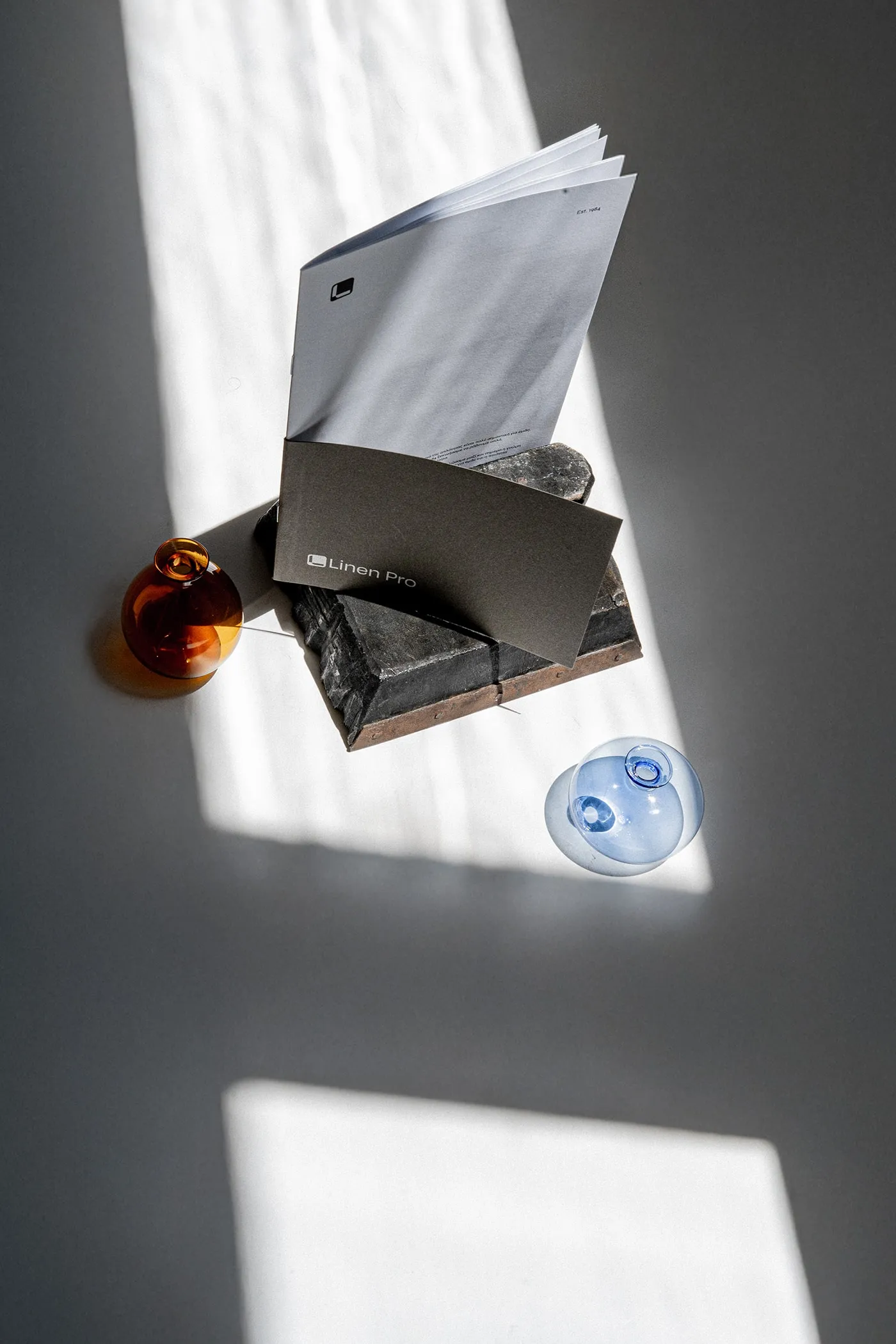 A grey folder and a pale blue booklet leaning on a dark brick between amber and blue glass globes
