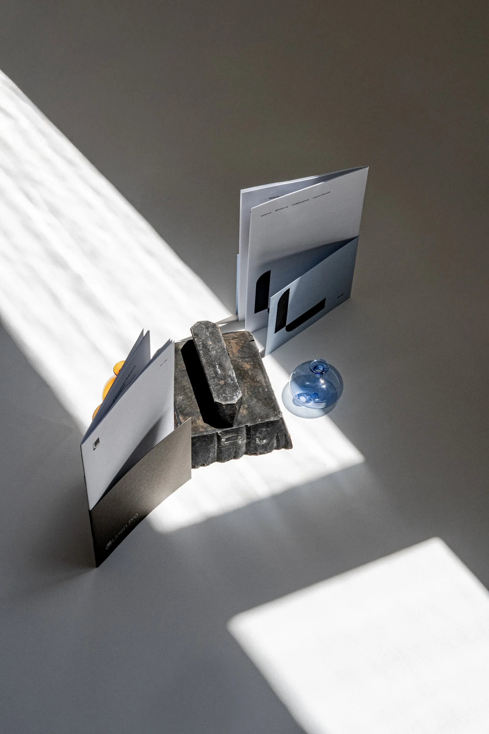 Folded Linen Pro leaflets standing against a dark brick in a band of sunlight