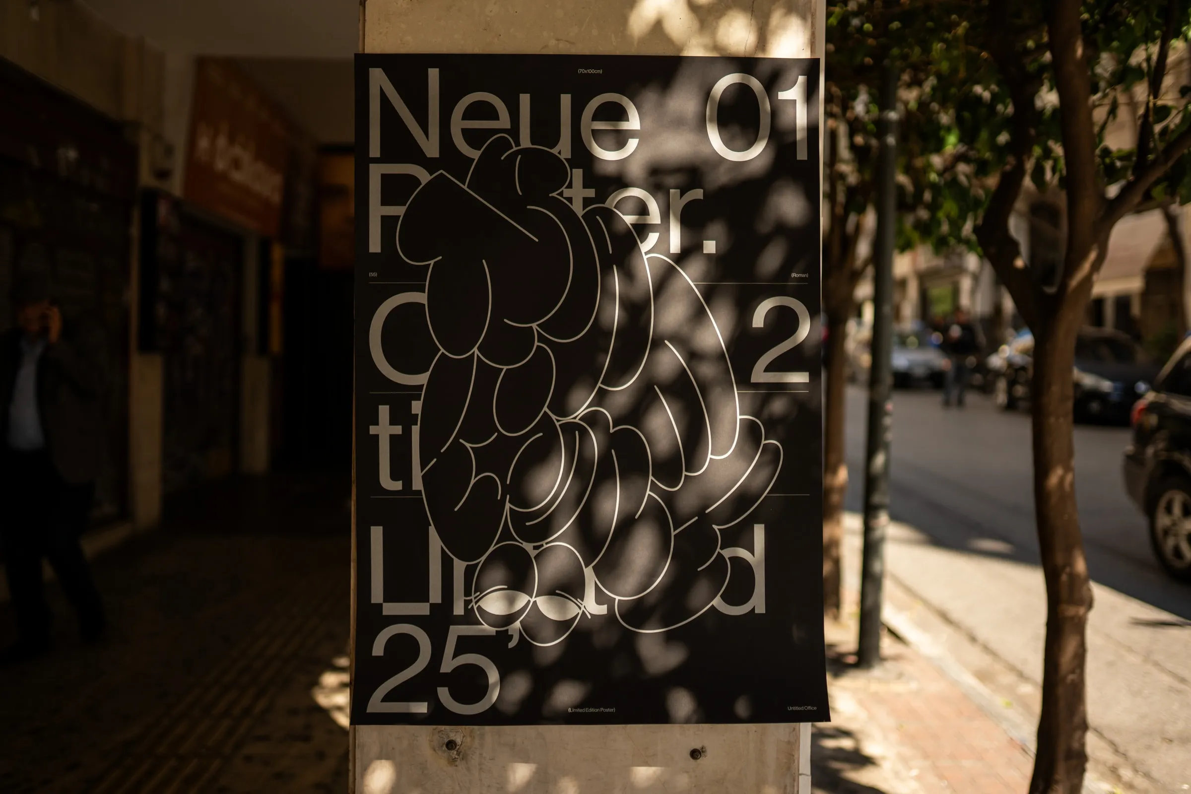 The Neue Poster 01 pasted on a pillar along a shaded city street