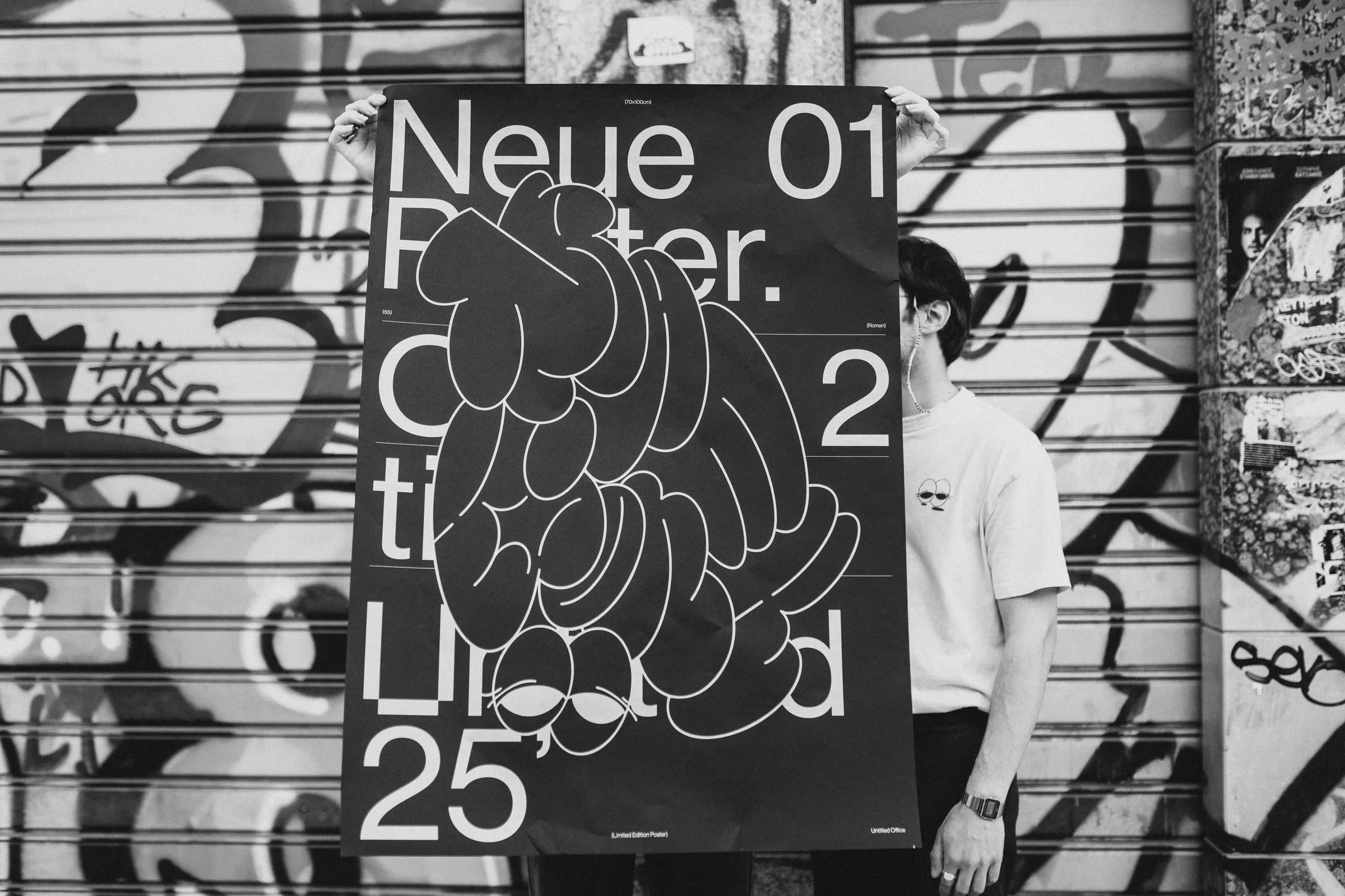 Black-and-white photo of the poster held up against a graffiti-covered shutter