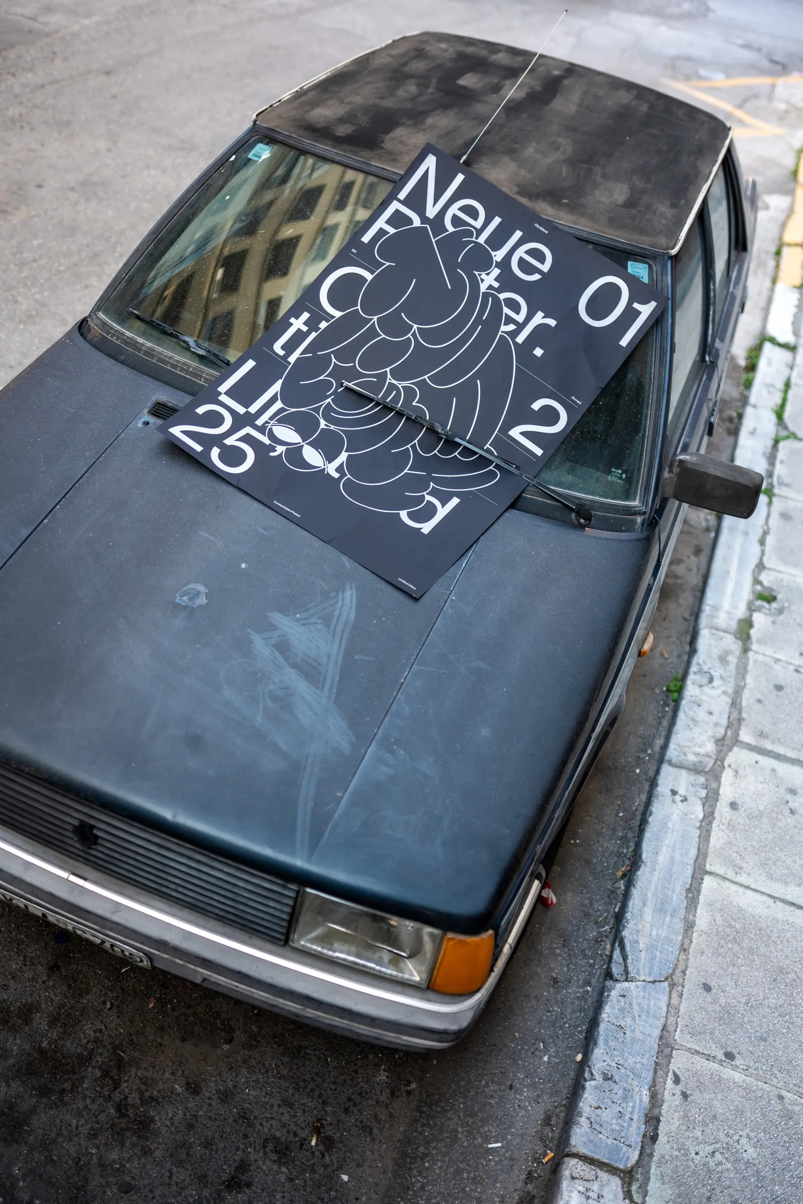 Overhead view of the poster lying on the roof and windscreen of a parked dark car