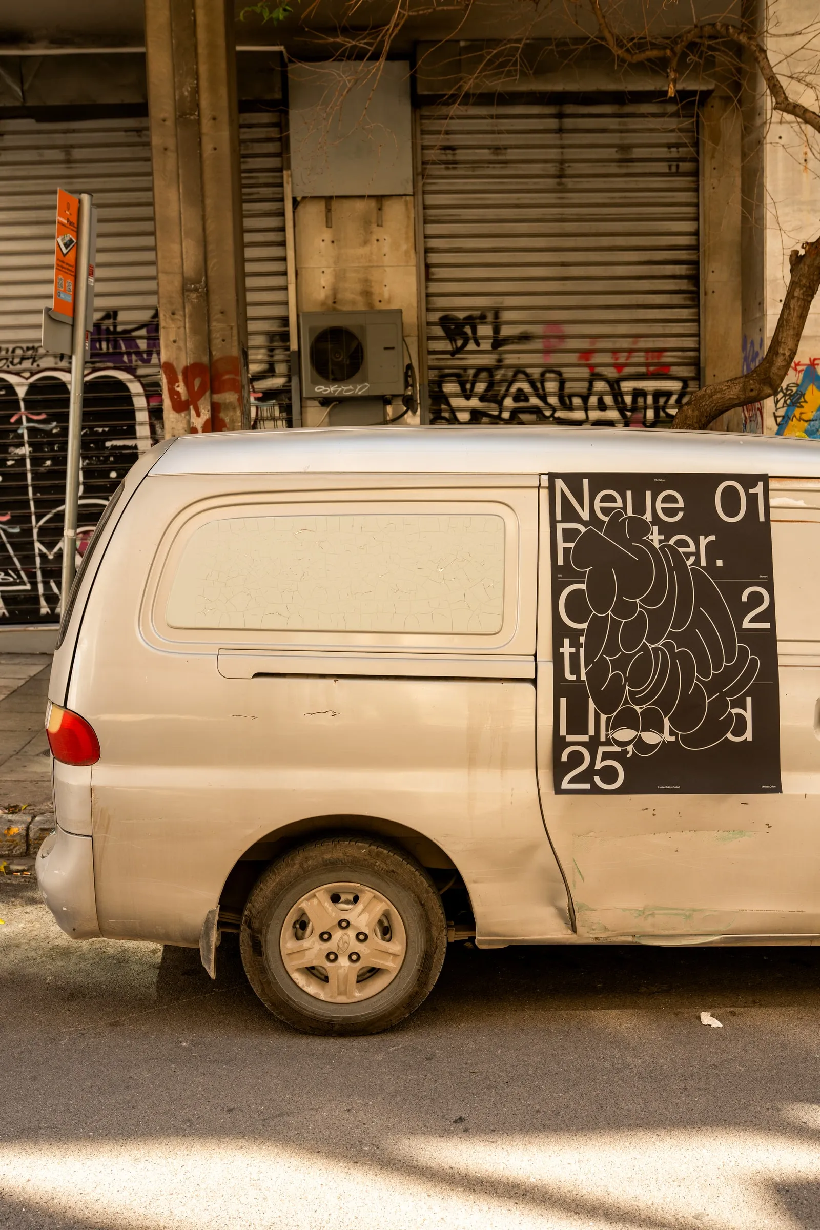 The poster stuck to the side of a white van in front of graffiti shutters
