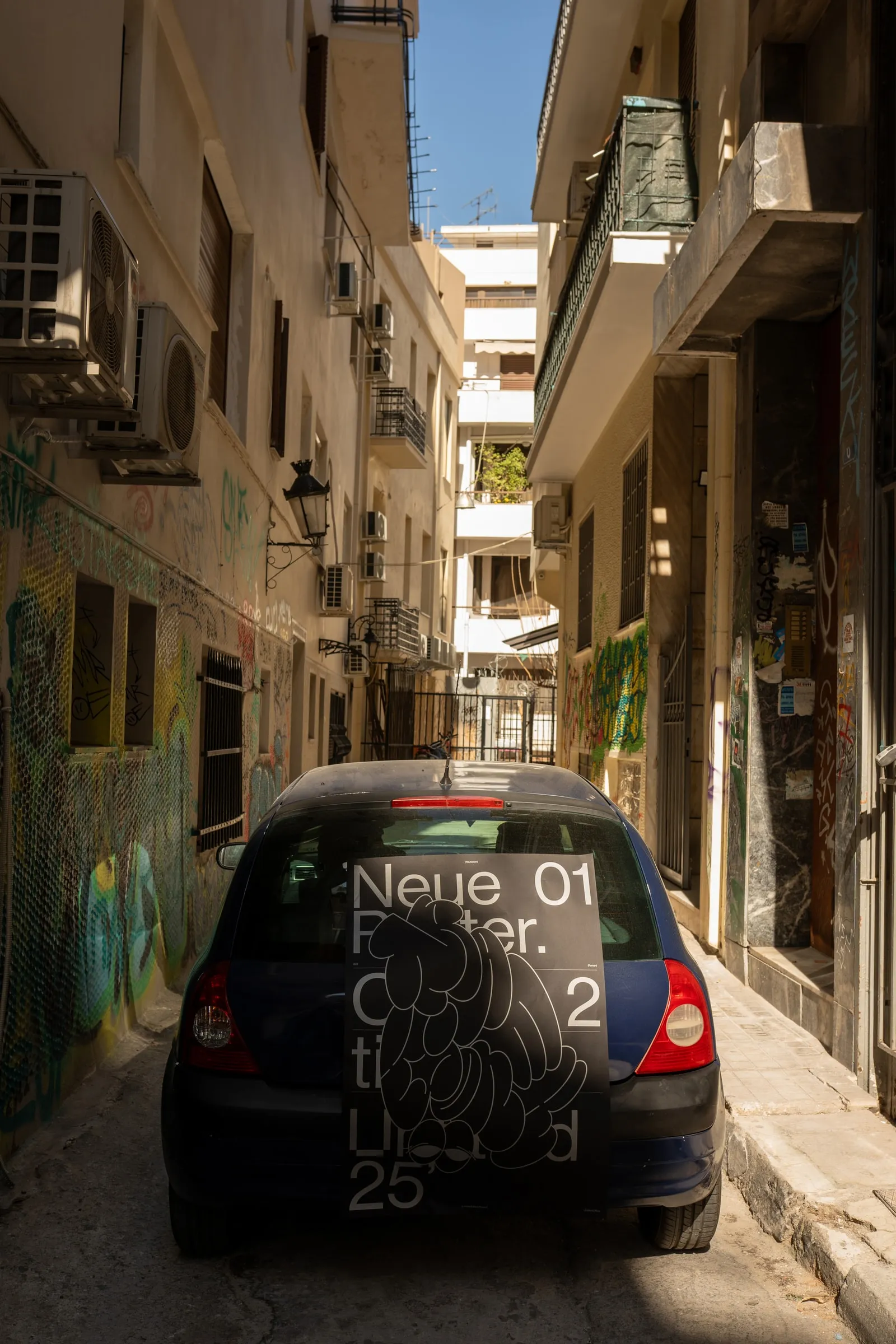 The poster on the rear window of a car parked in a narrow street