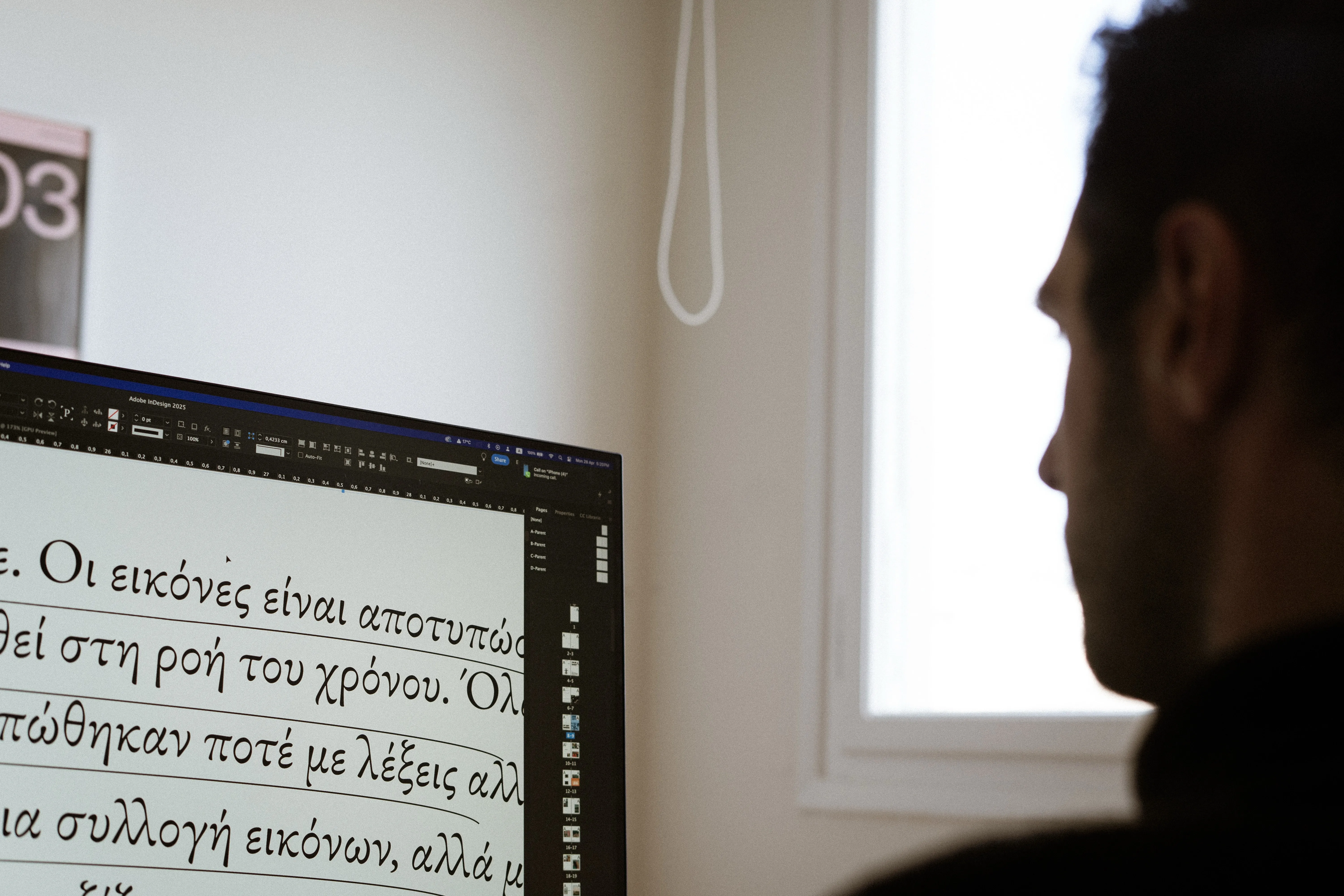 Over-the-shoulder view of a silhouetted designer looking at Greek typesetting on a large monitor