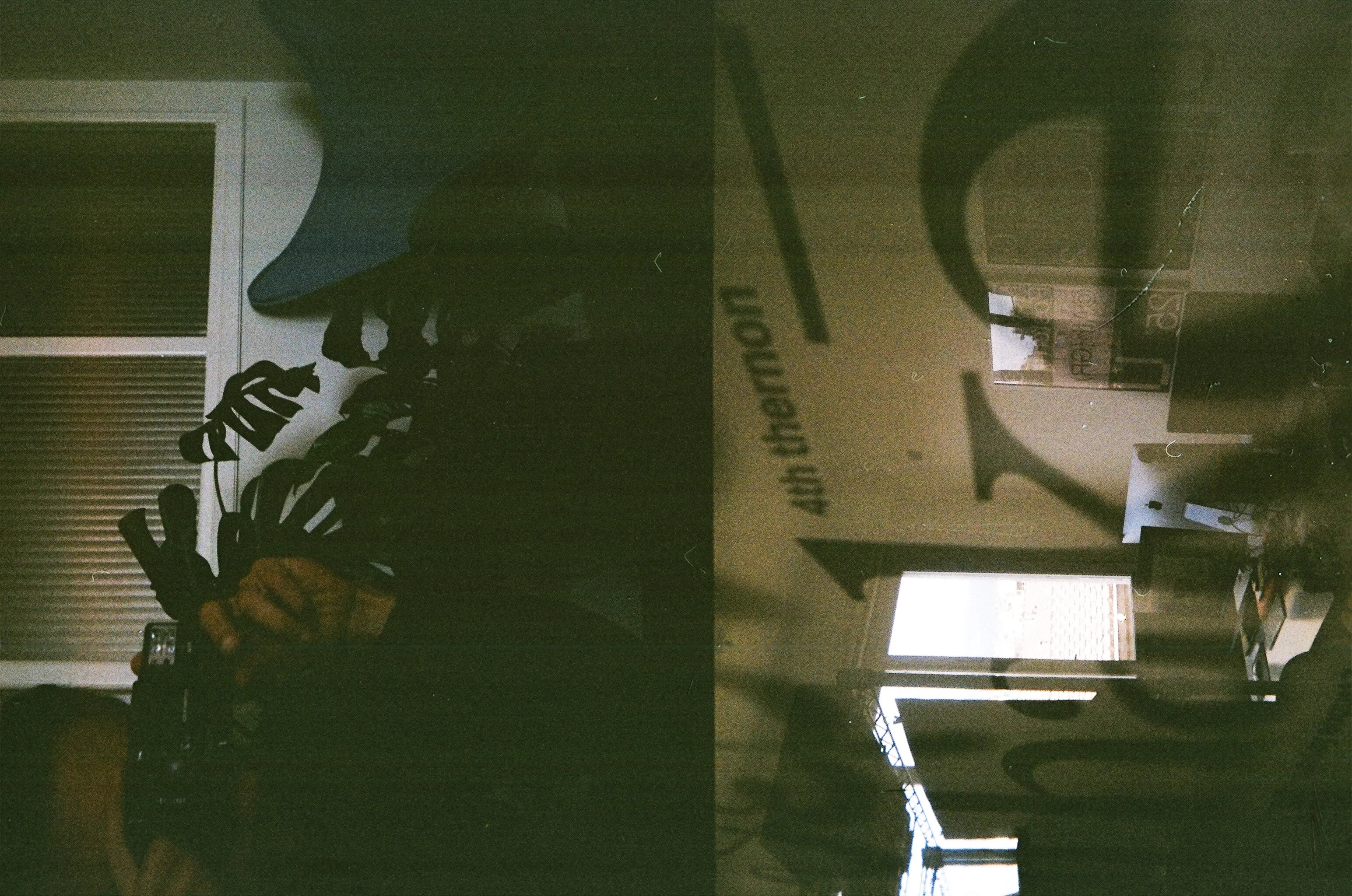 Double-exposed film photo of the studio: monstera leaves, a window blind and large lettering on the wall