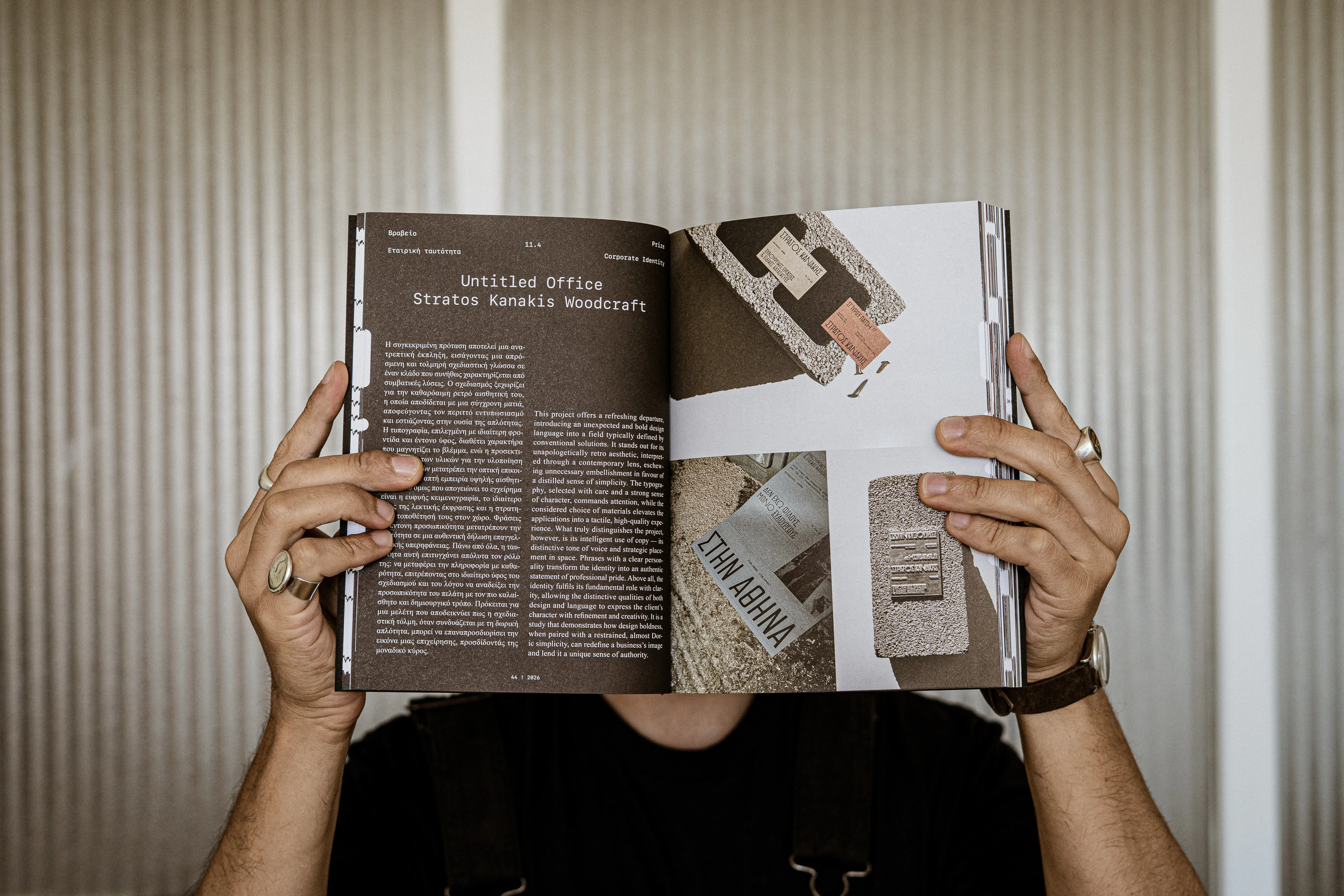 An open magazine spread about a corporate identity project, held up in front of a ribbed wall