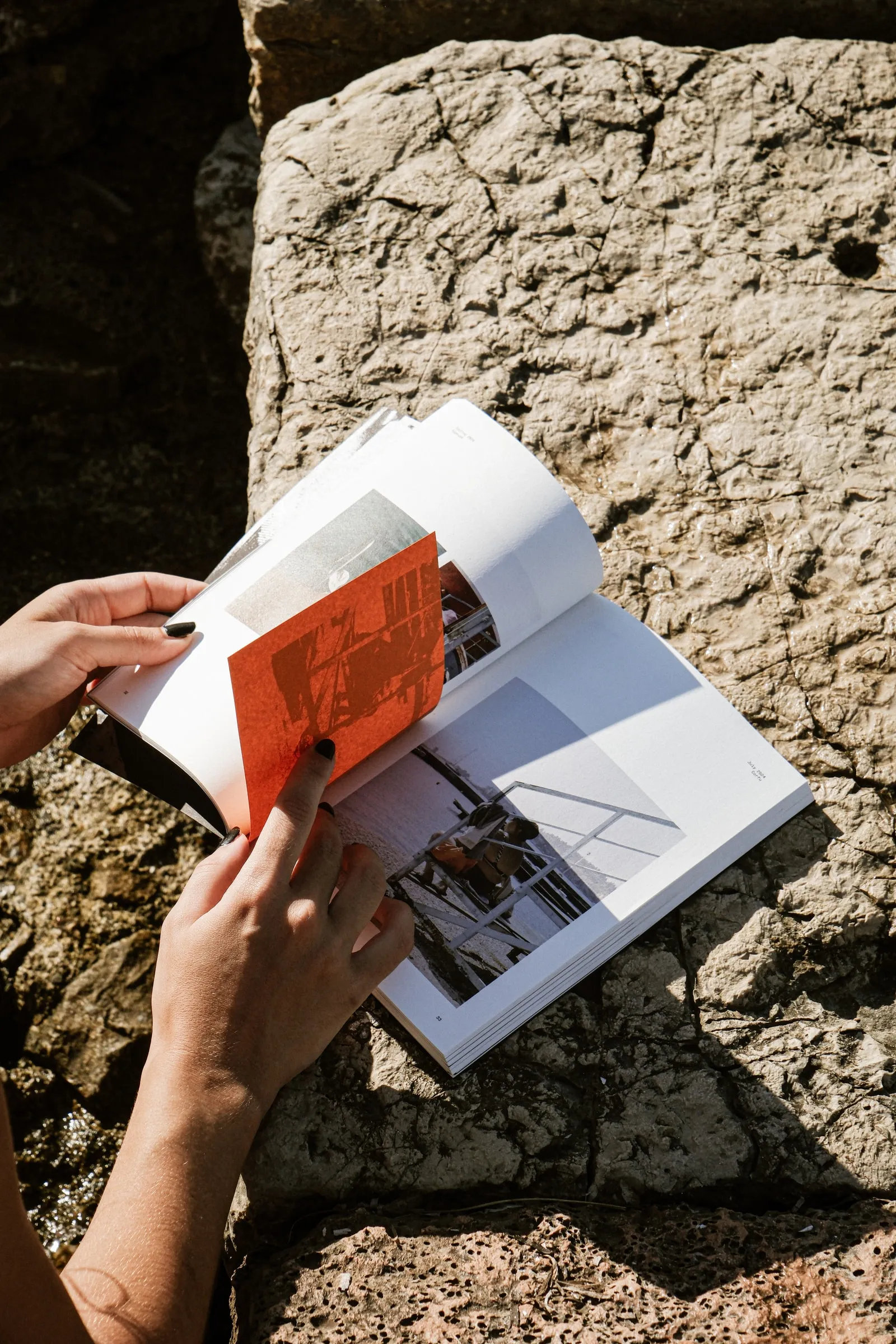 Hands leafing through the open photobook on a sunlit stone ledge