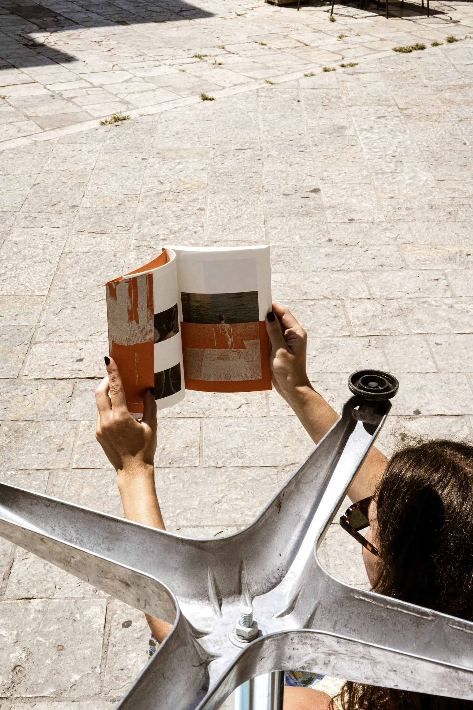 Someone holding the open photobook up against the sun above a metal chair base