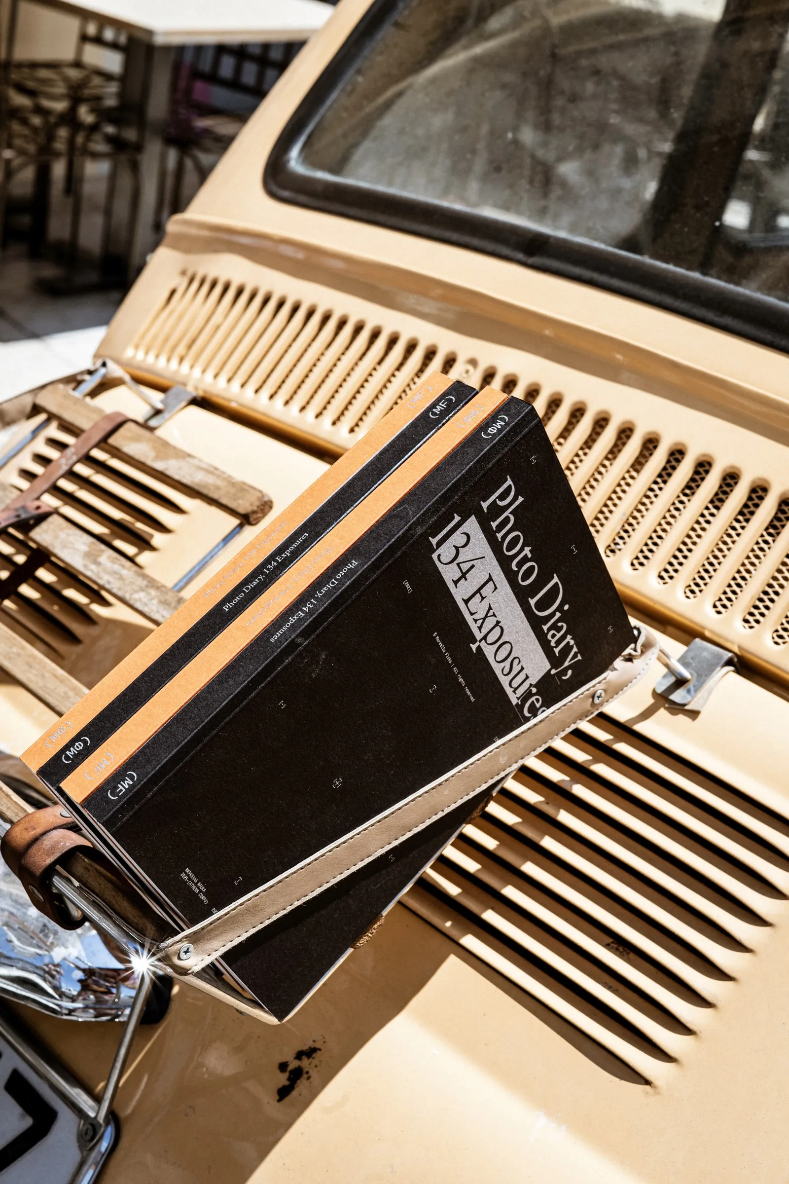 The photobook resting on the louvred rear grille of a cream vintage car