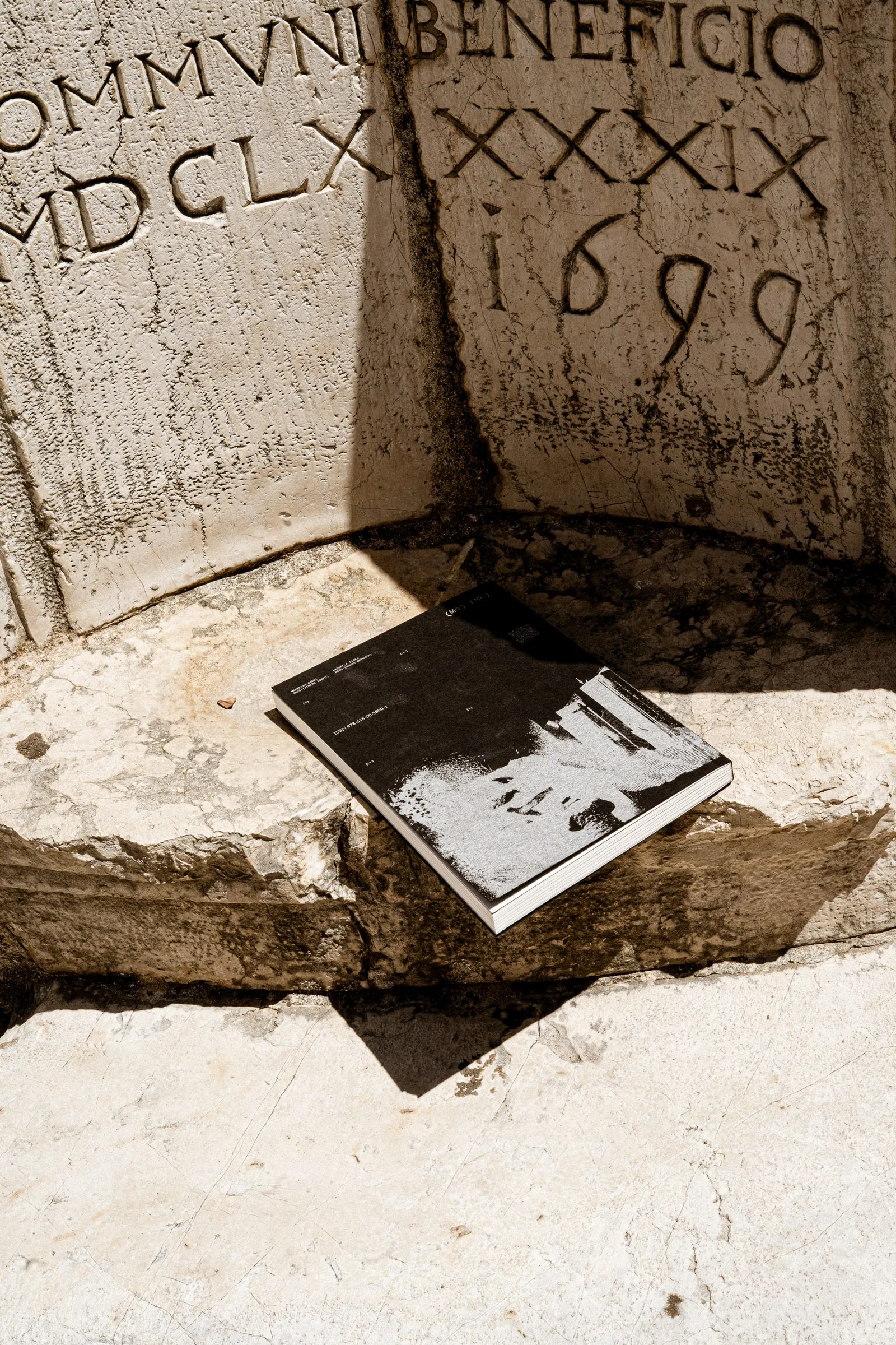 The photobook on a stone ledge below a carved Latin inscription dated 1699