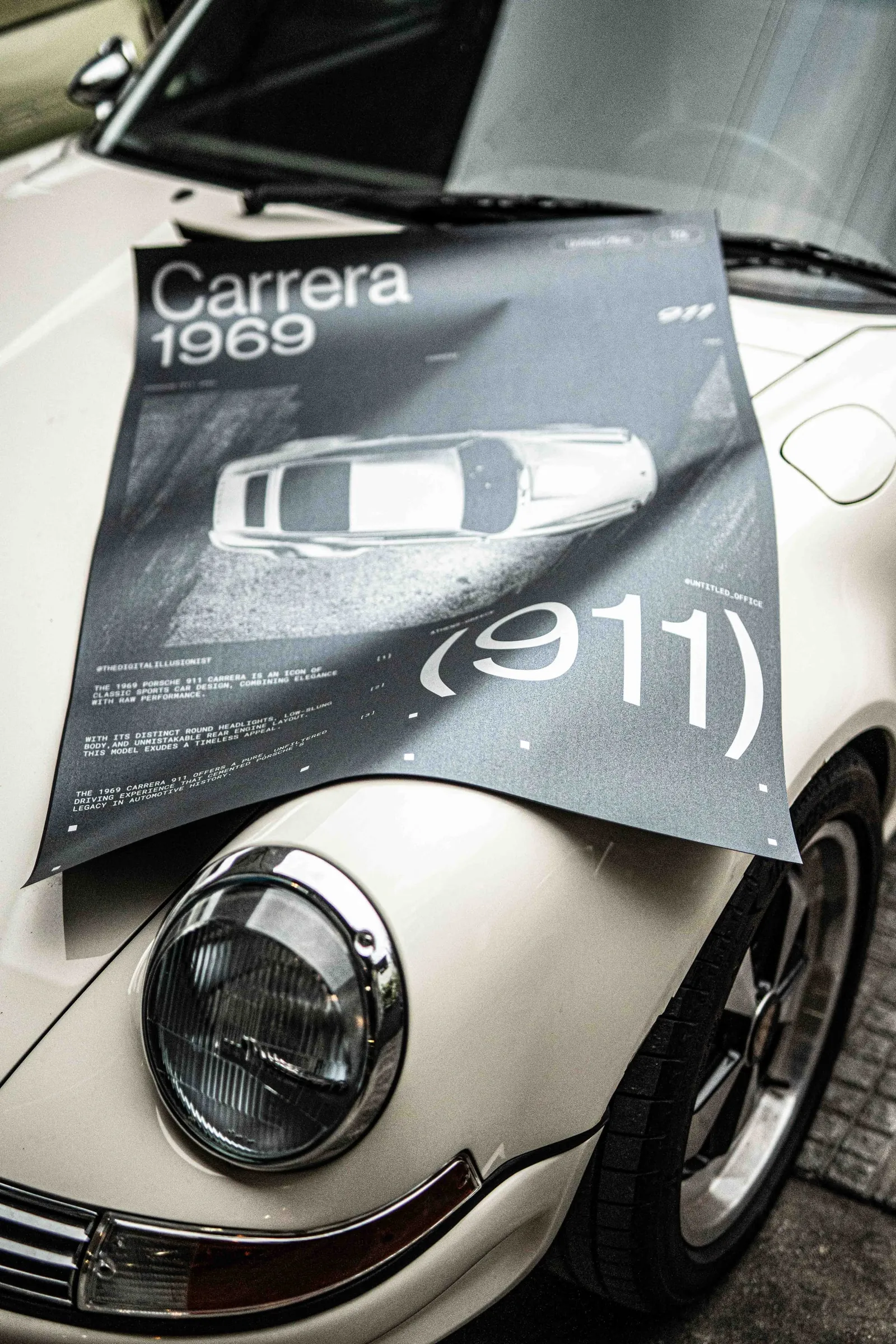 The Carrera 1969 poster draped over the front of a white Porsche 911 beside its headlight