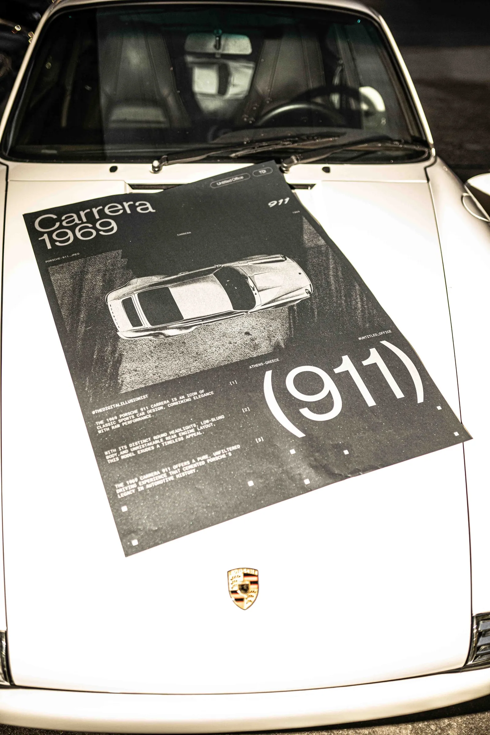 The poster lying on the bonnet of a white Porsche 911 above the crest