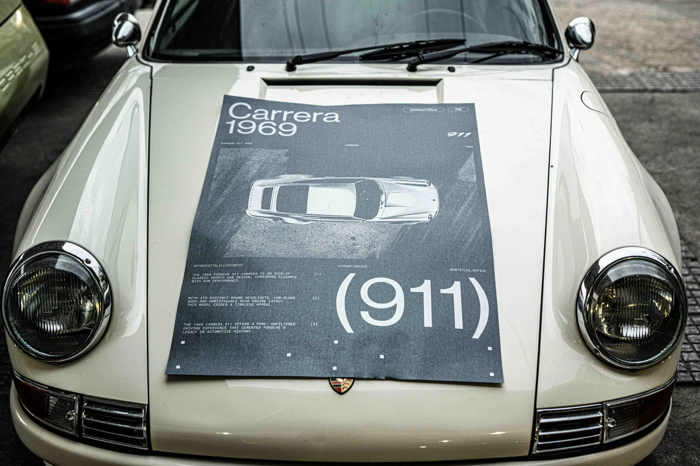 Head-on view of the poster laid across the bonnet of a white Porsche 911