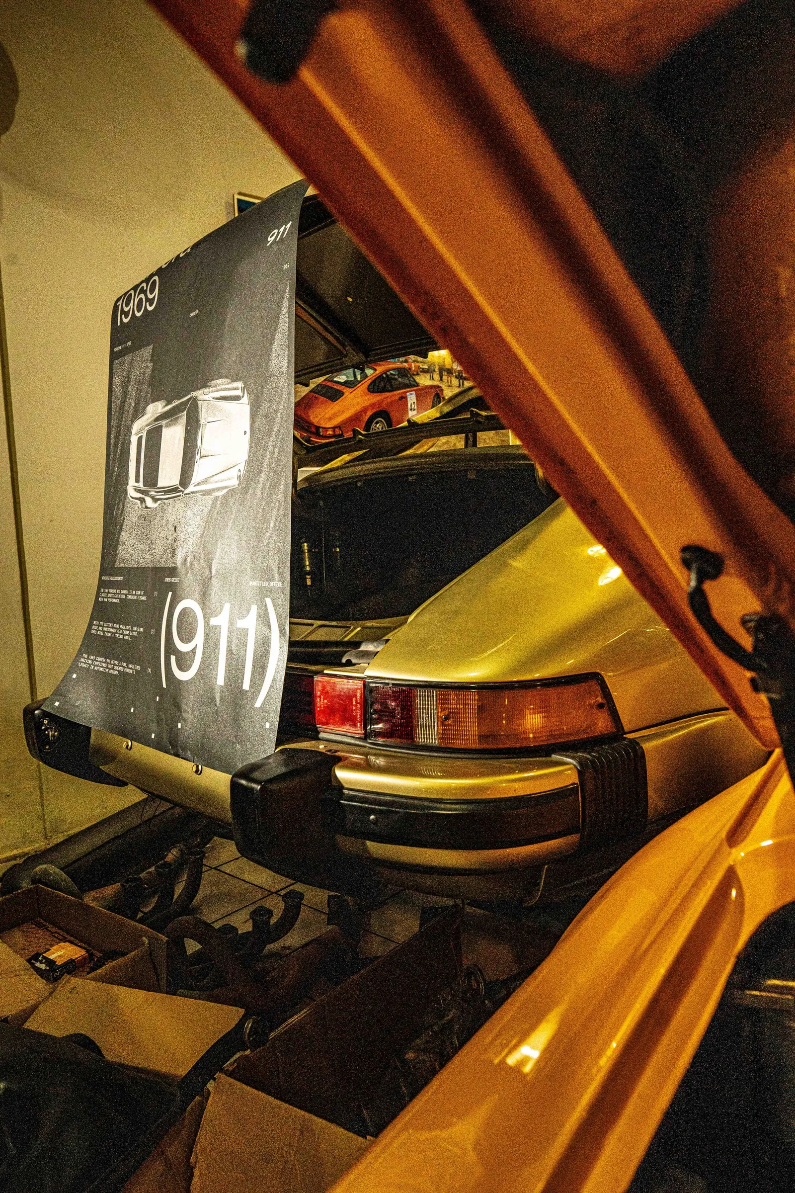 The poster hanging inside the raised engine lid of a yellow 911, in warm light