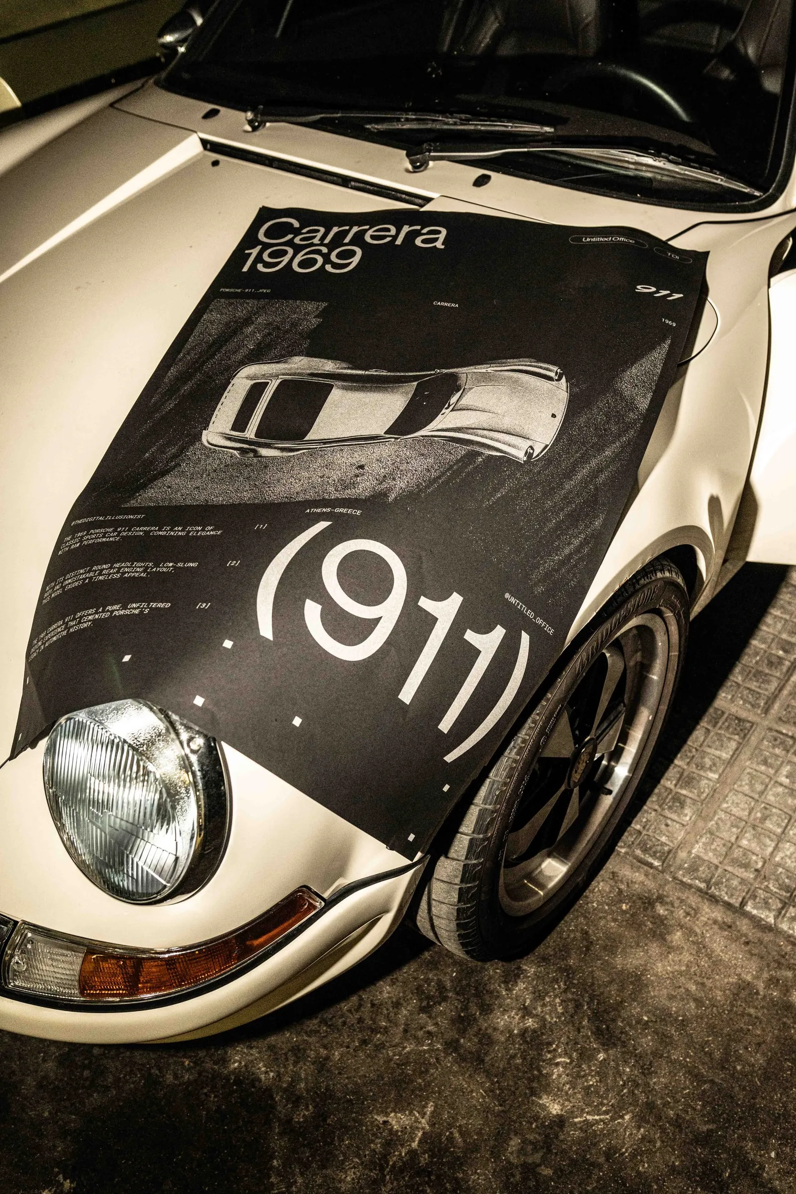 The poster on the bonnet of a white Porsche 911 next to its round headlight