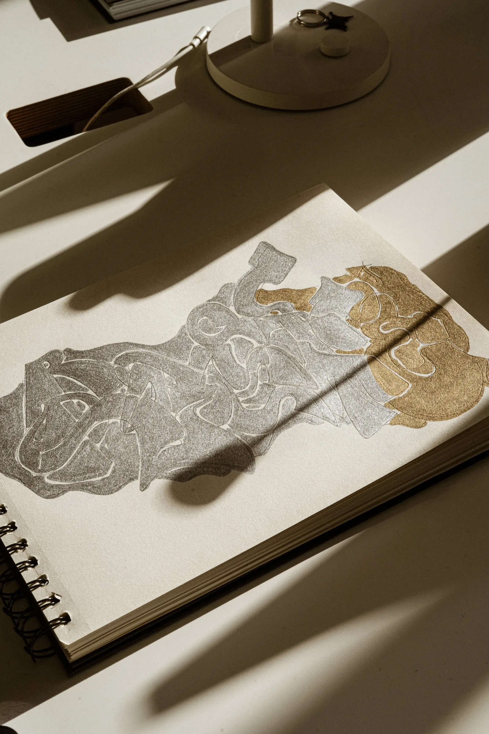 An open spiral sketchbook with an abstract silver and gold drawing, in raking afternoon light
