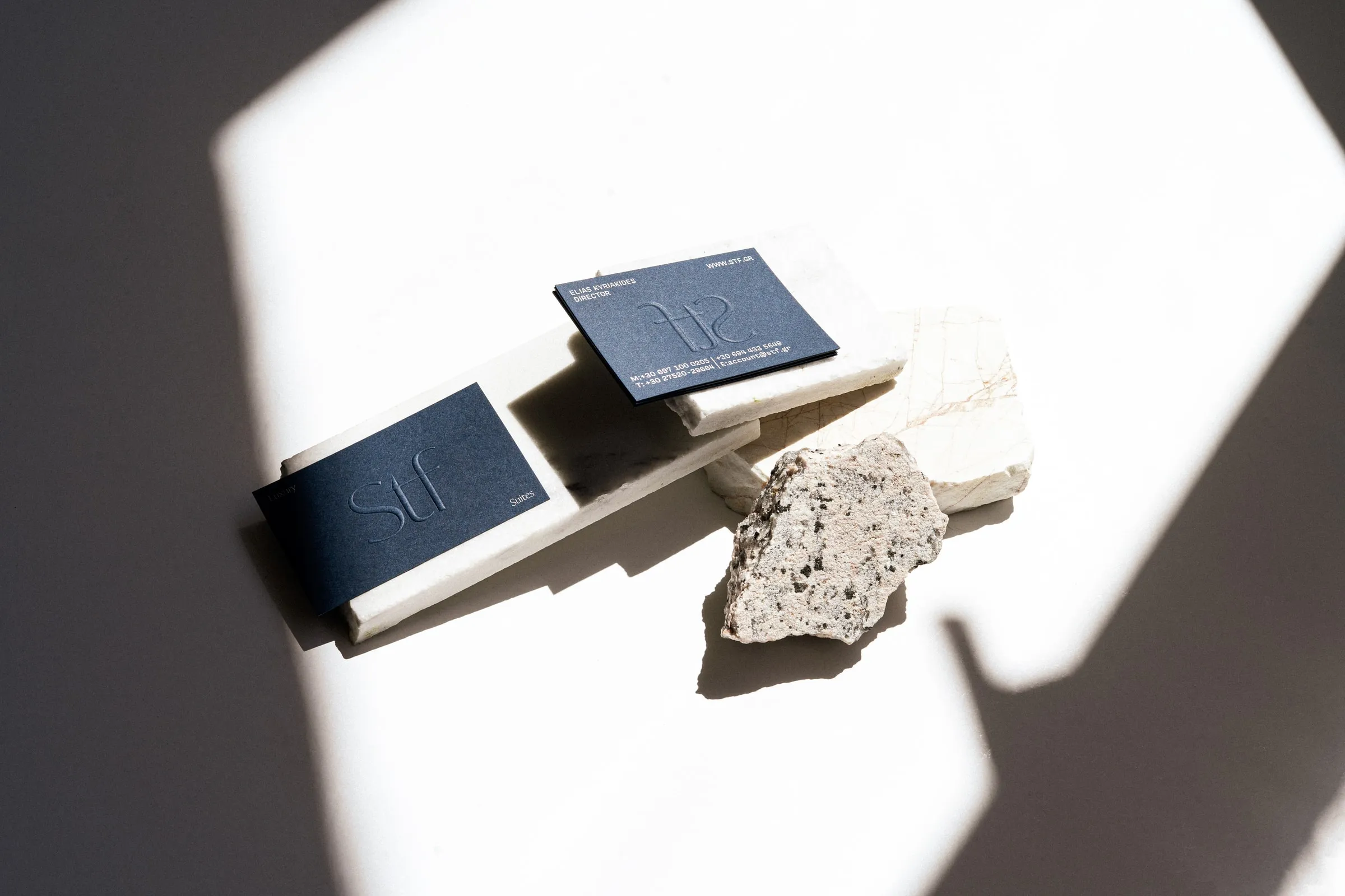 Navy STF business cards on white marble slabs beside a speckled granite stone