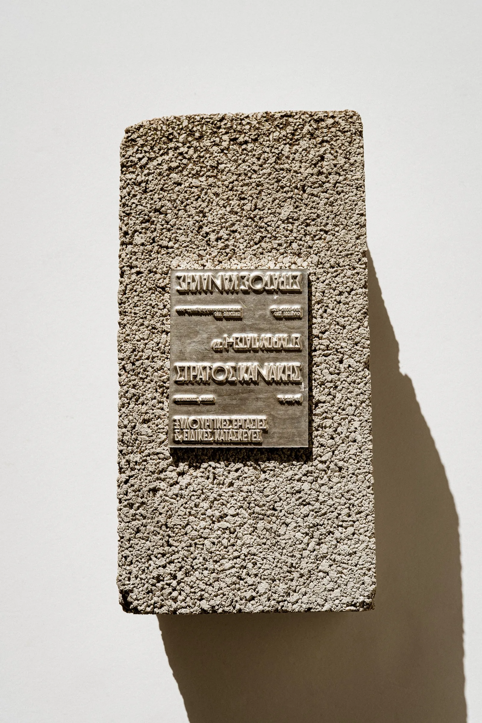 An embossed metal plate with Greek lettering set into a concrete block, in hard sunlight