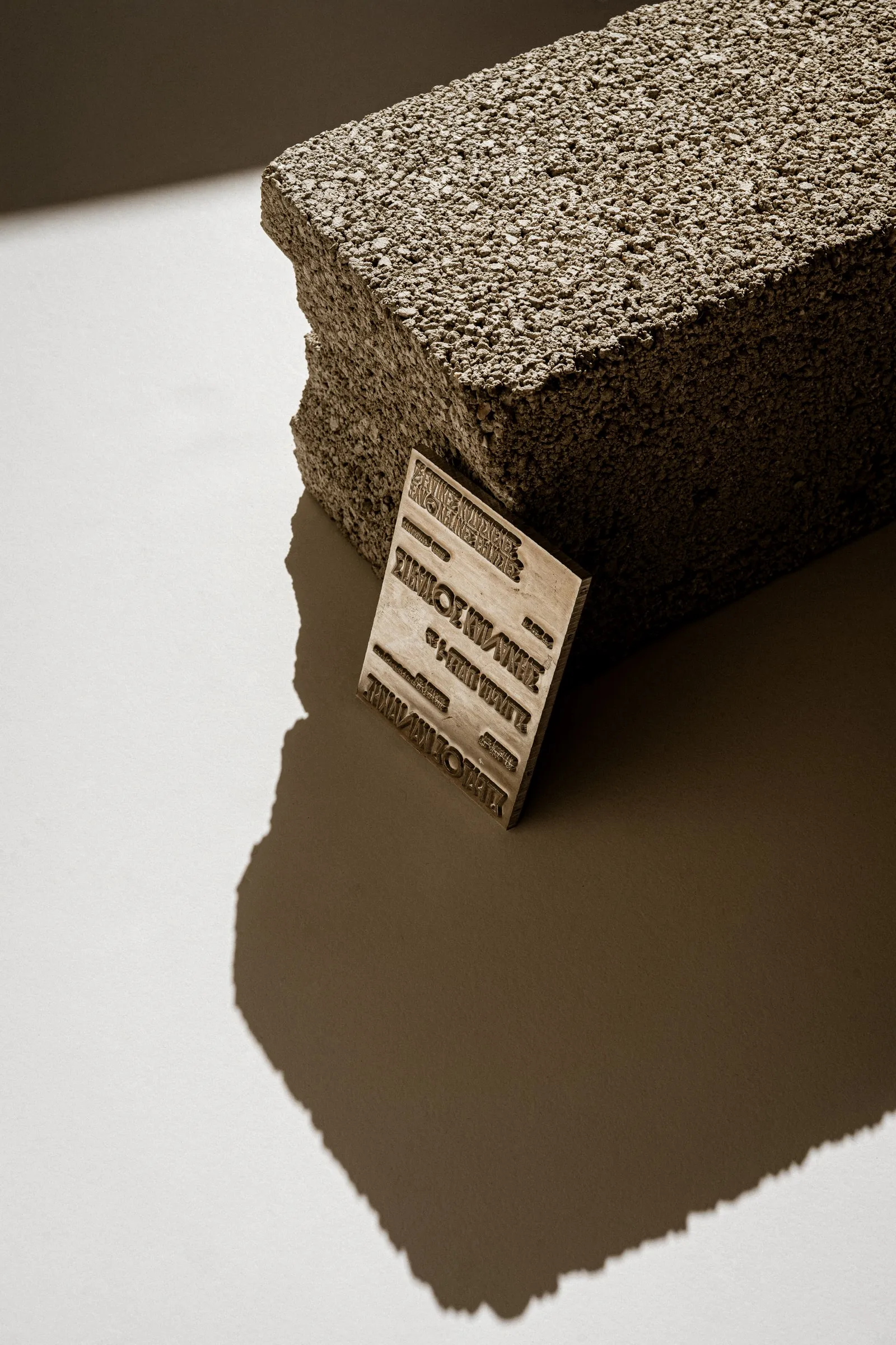 The embossed metal plate leaning against a concrete block, casting a long shadow