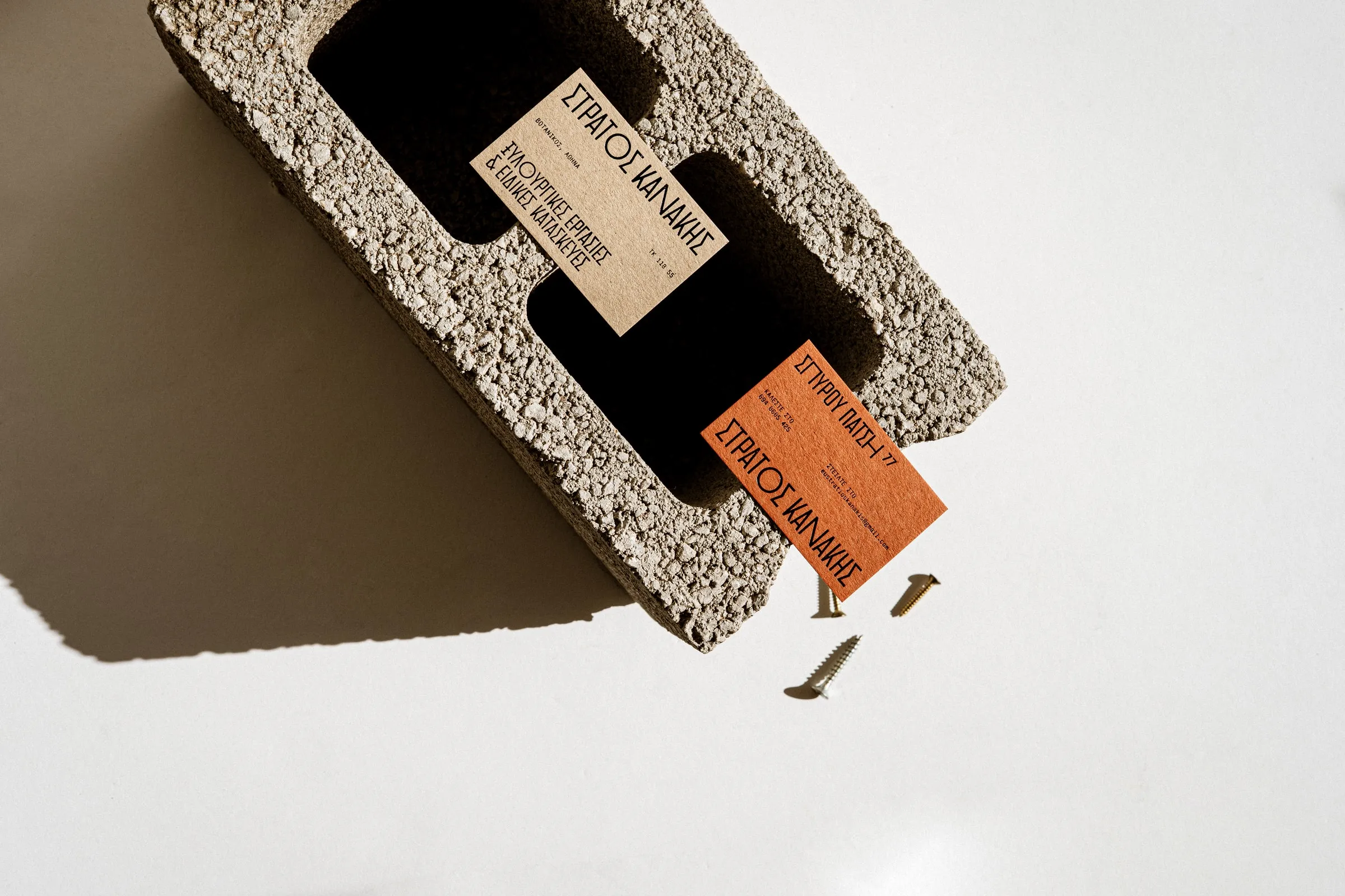 A cream card and an orange business card tucked into a hollow concrete block, with brass screws