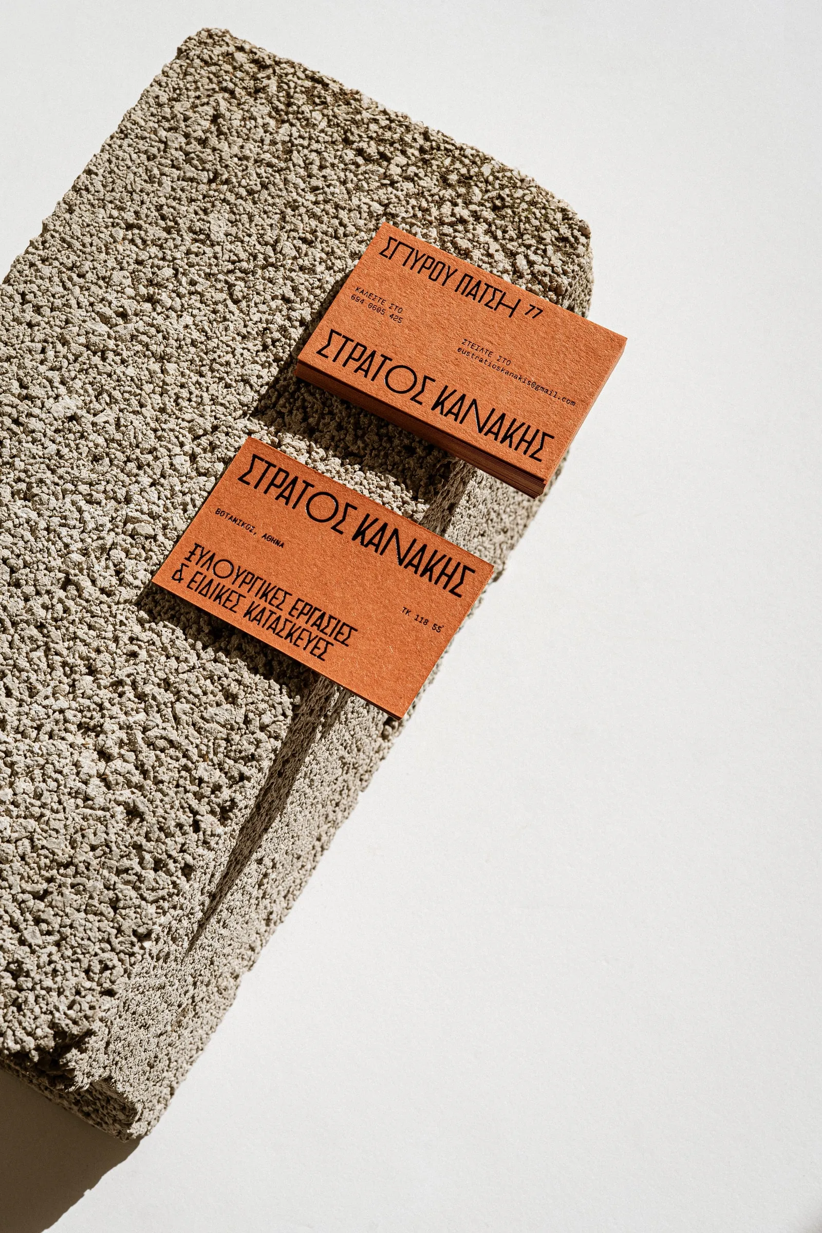 Two orange business cards with black Greek lettering on a concrete block