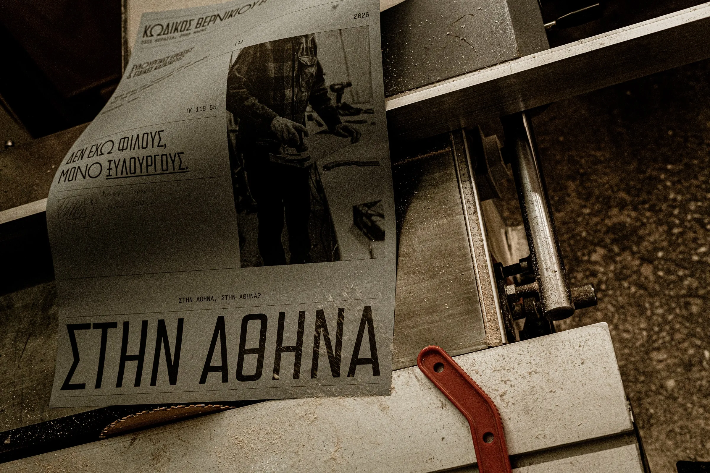 A ΣΤΗΝ ΑΘΗΝΑ poster lying across a saw bench beside an orange handle