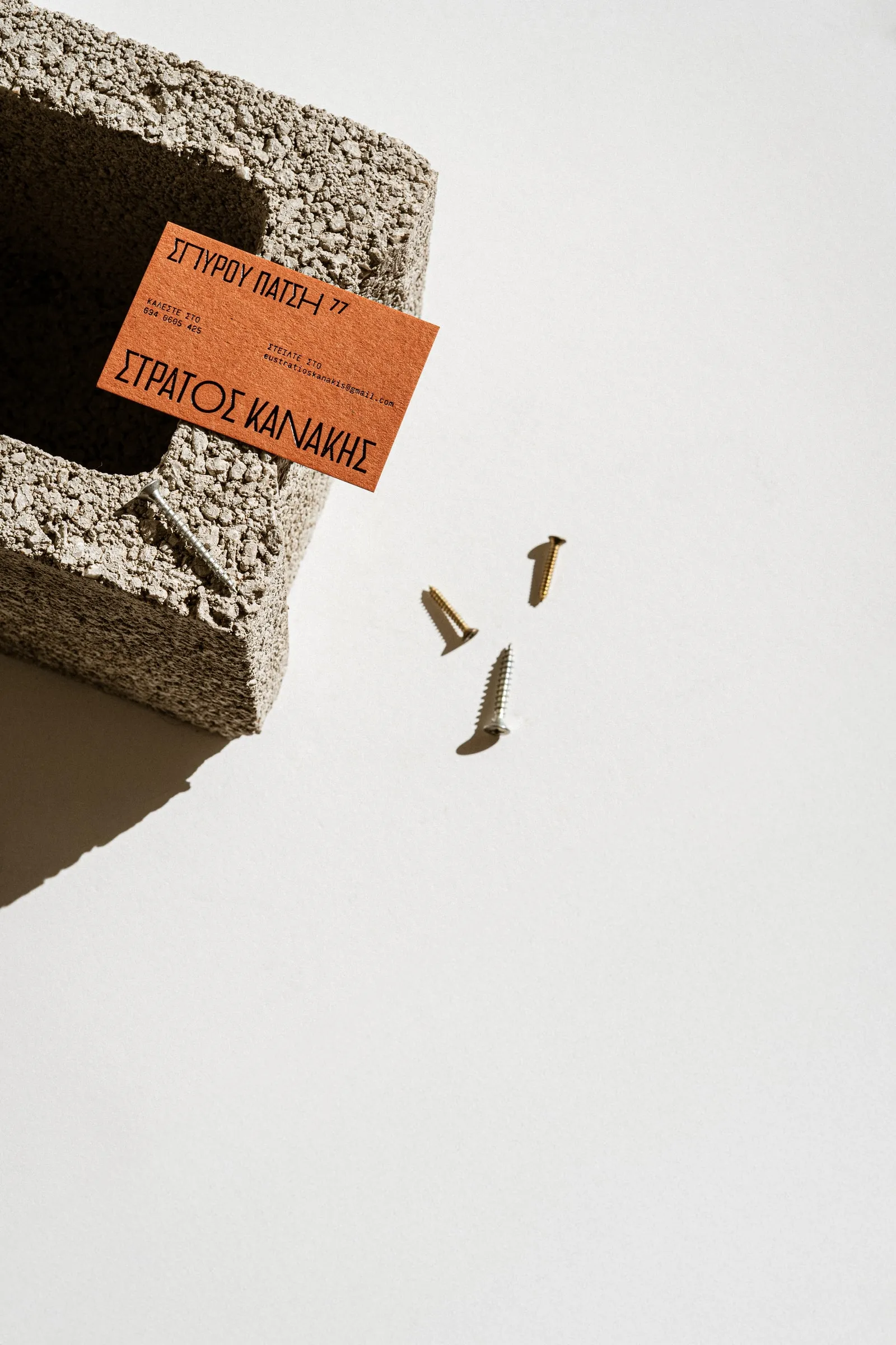An orange business card on the corner of a concrete block, brass screws scattered beside it