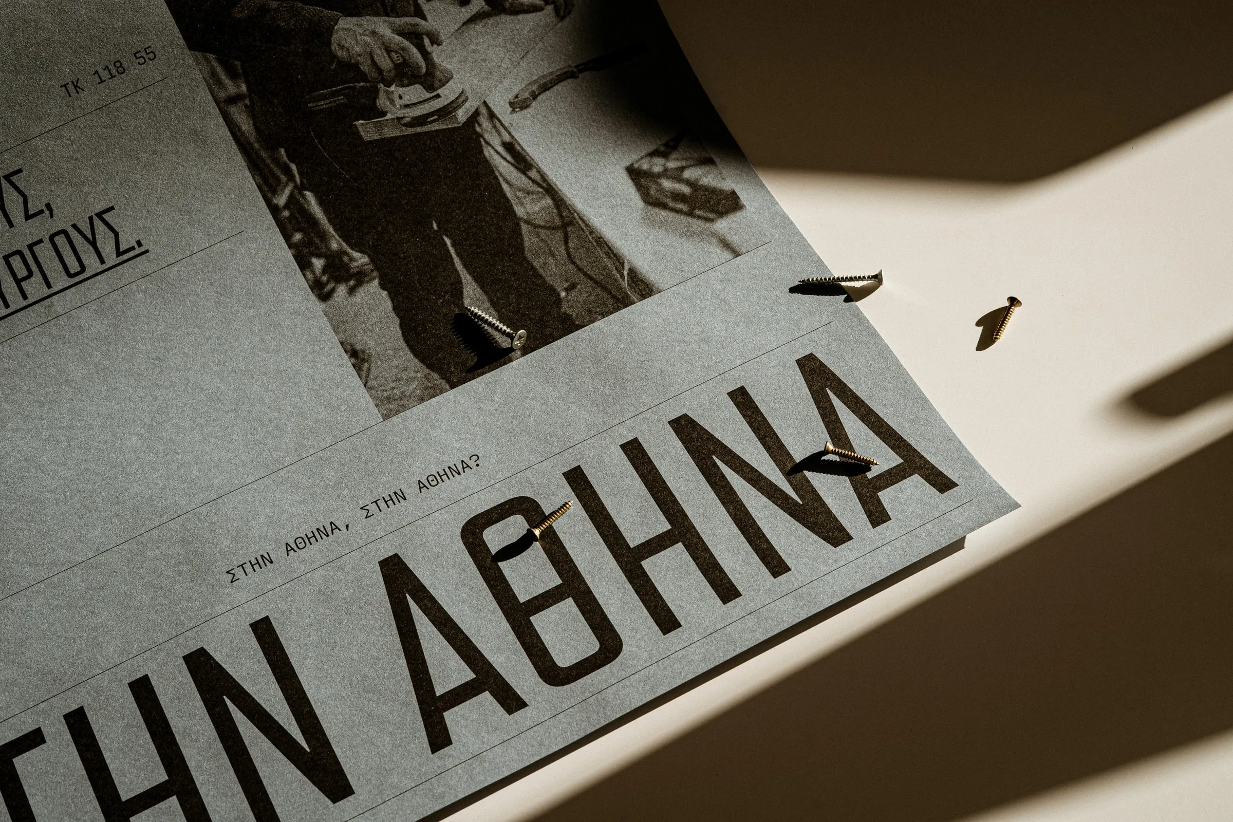 Close-up of the ΣΤΗΝ ΑΘΗΝΑ poster in sunlight, with two brass screws resting on it