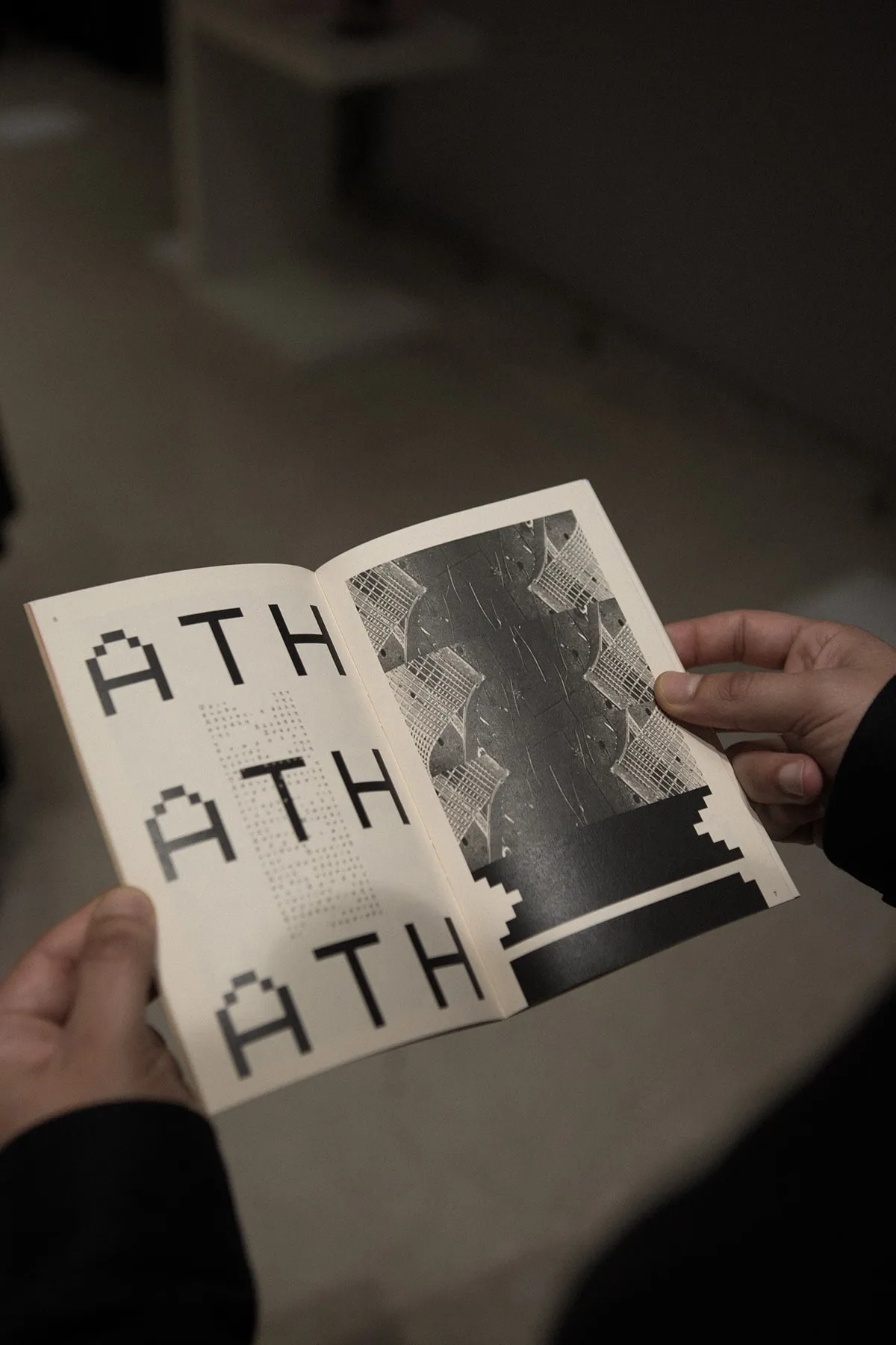 Hands holding the zine open at pages of repeated ATH lettering