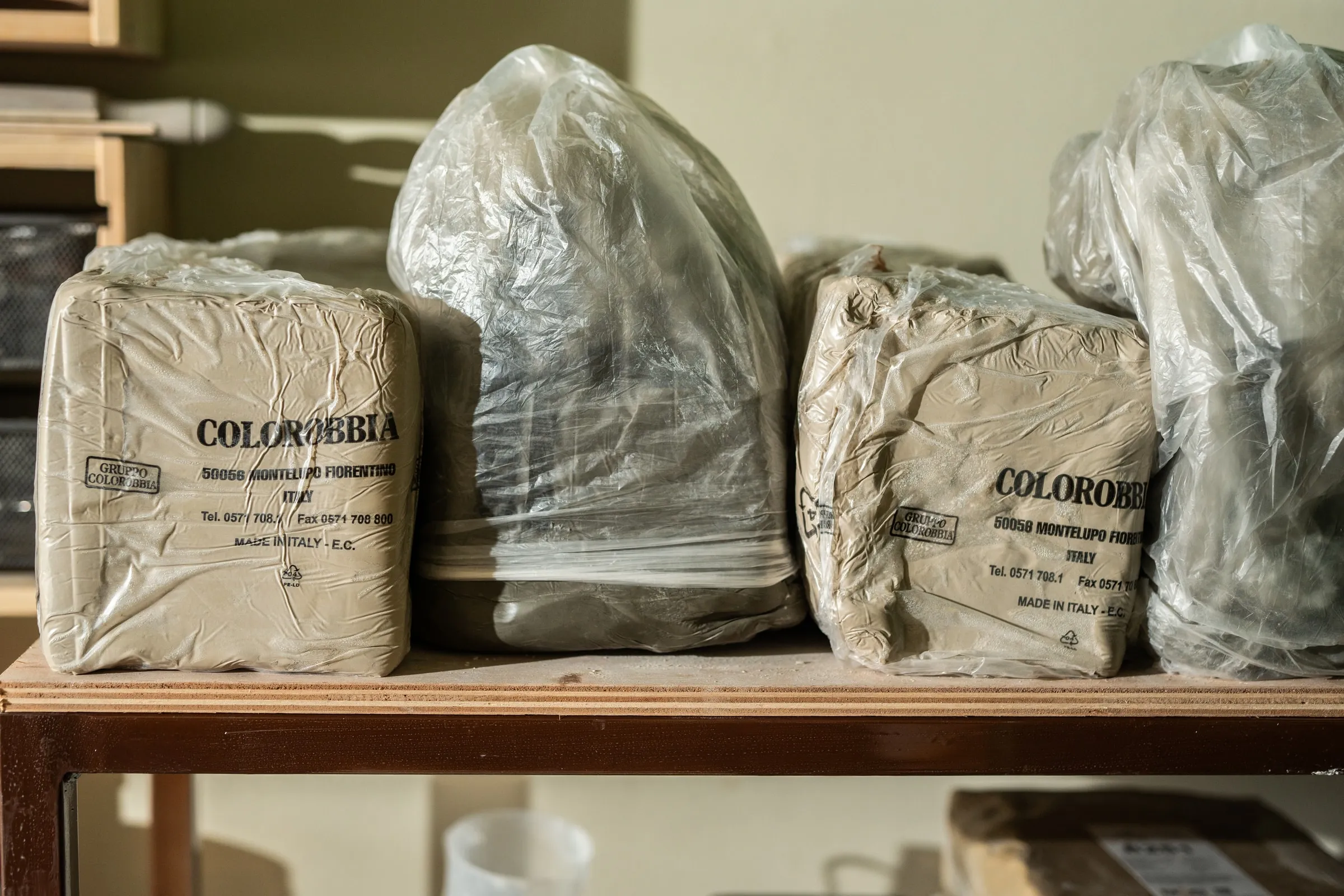 Blocks of clay wrapped in plastic on a wooden studio shelf
