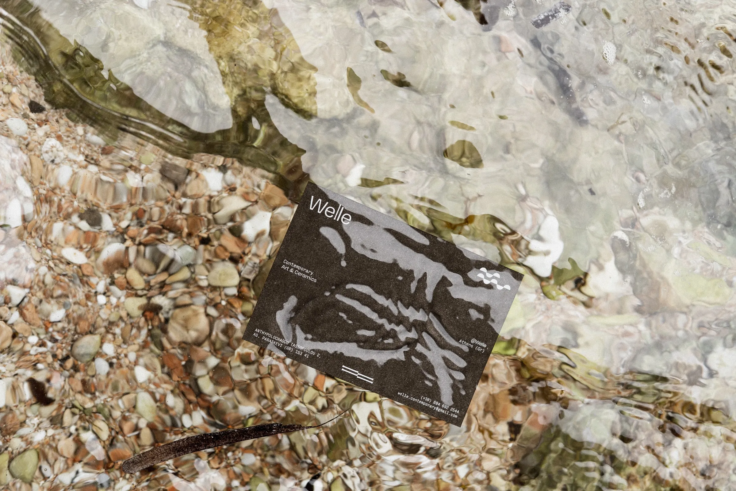 A dark Welle postcard lying in shallow clear water over pebbles