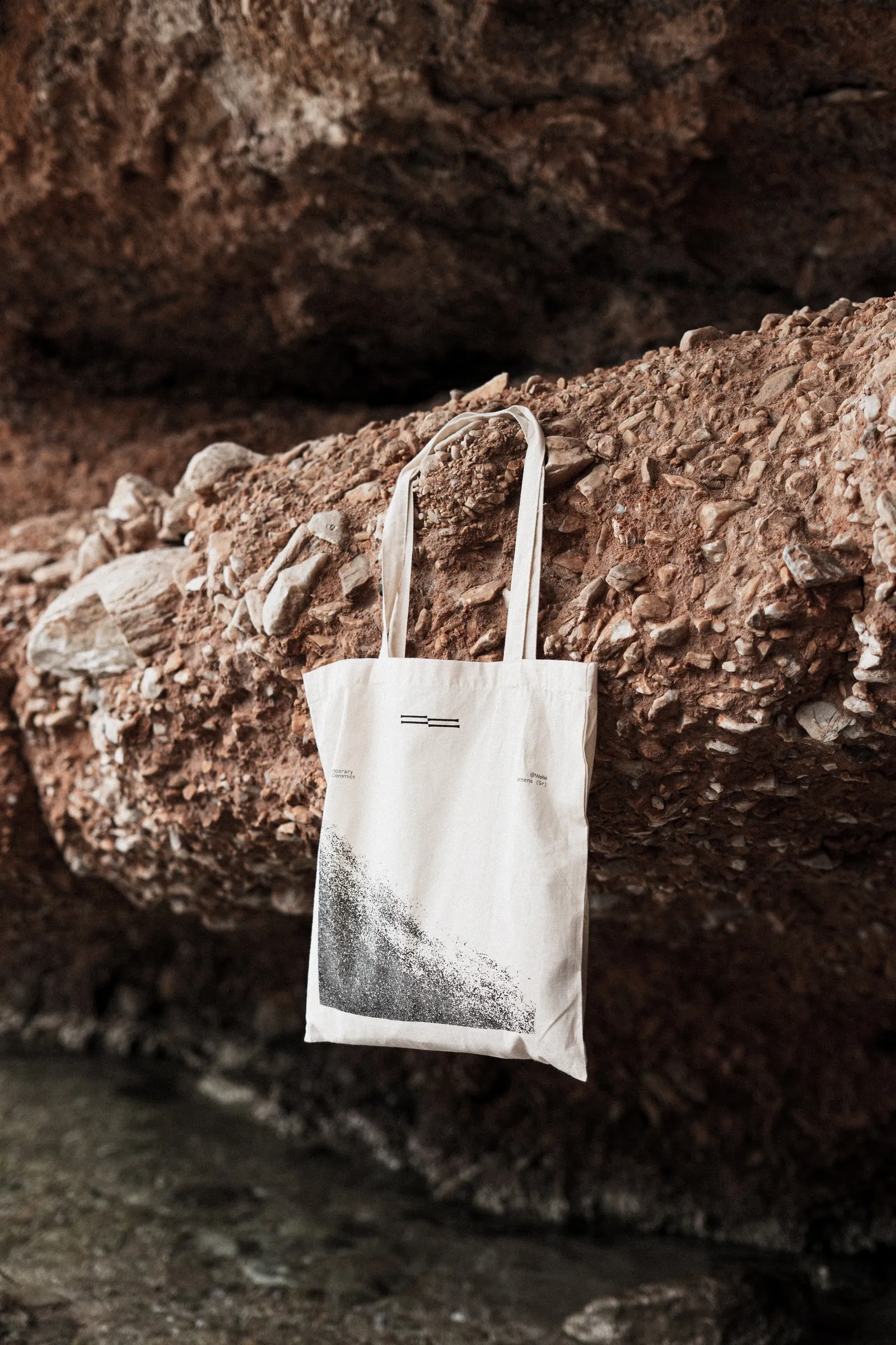 A cream Welle tote bag with a black print, hanging from a red rock ledge