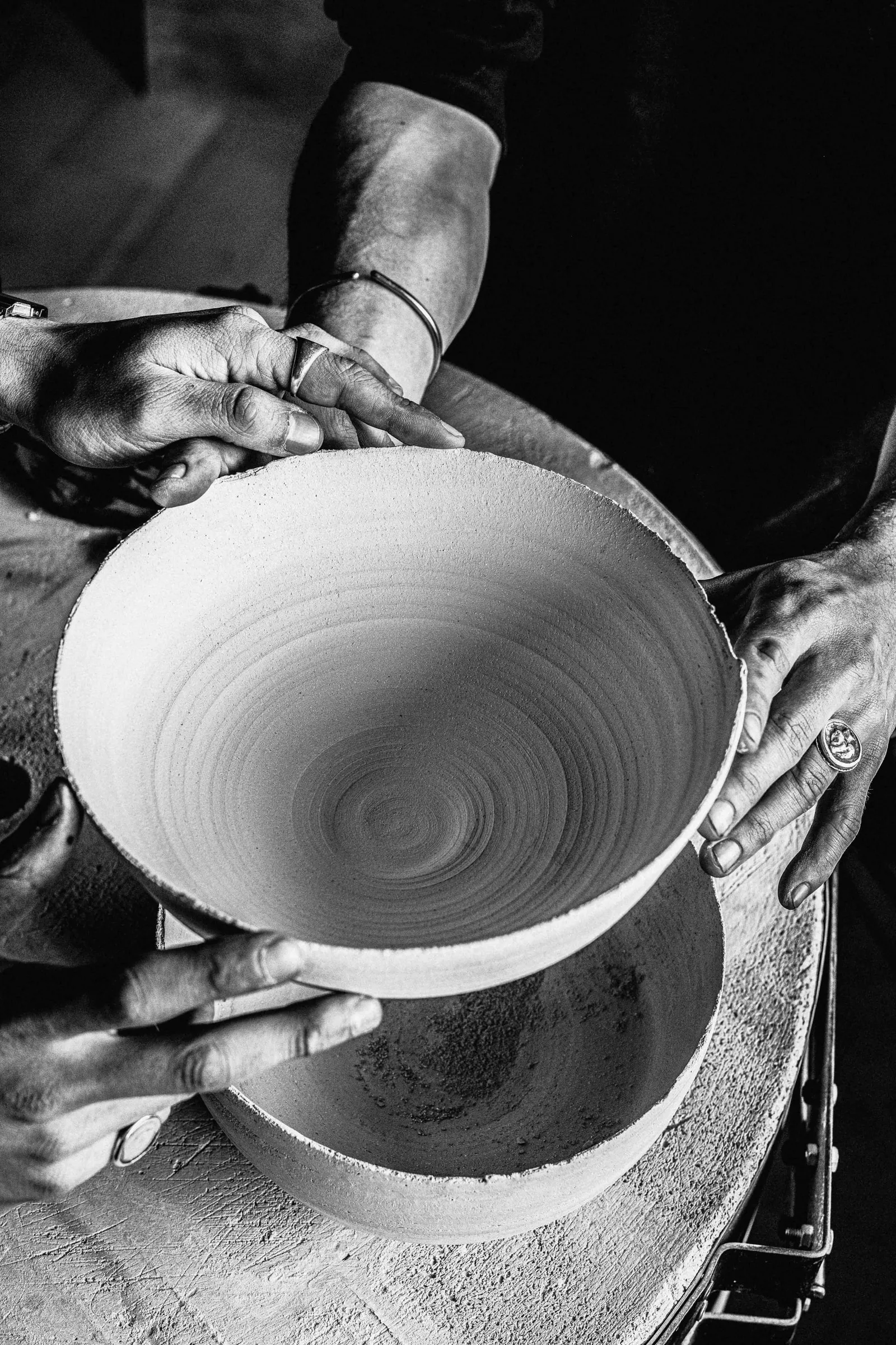 Black-and-white photo of hands holding a freshly thrown clay bowl above the wheel